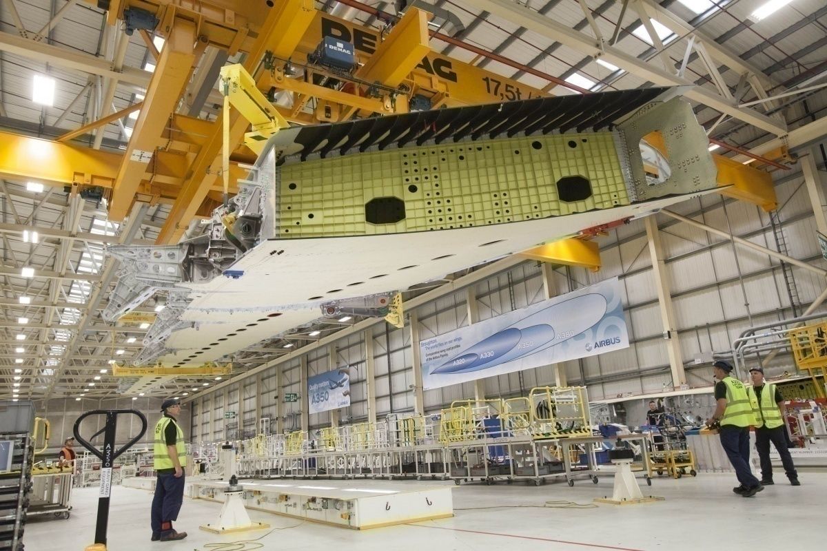 Part of a wing of an Airbus A350 being lifted by a machine inside a manufacturing plant.