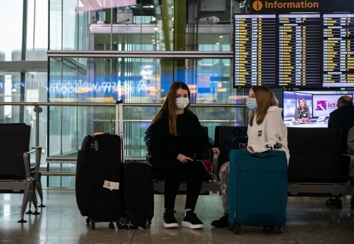 Two girls in masks sit at airport