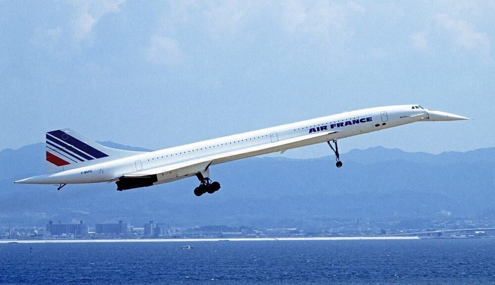 An Air France Concorde flying over water with mountains in the background.
