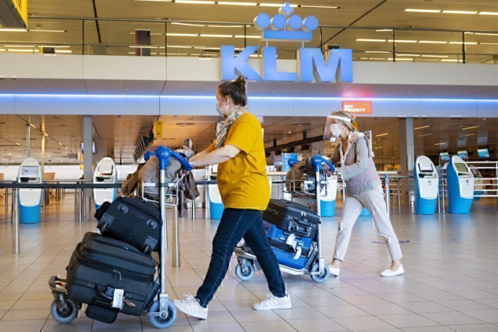 Travelers wearing a face mask walk by KLM check-in