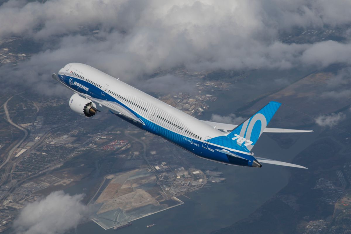 A Boeing 787 in house livery flying over land.
