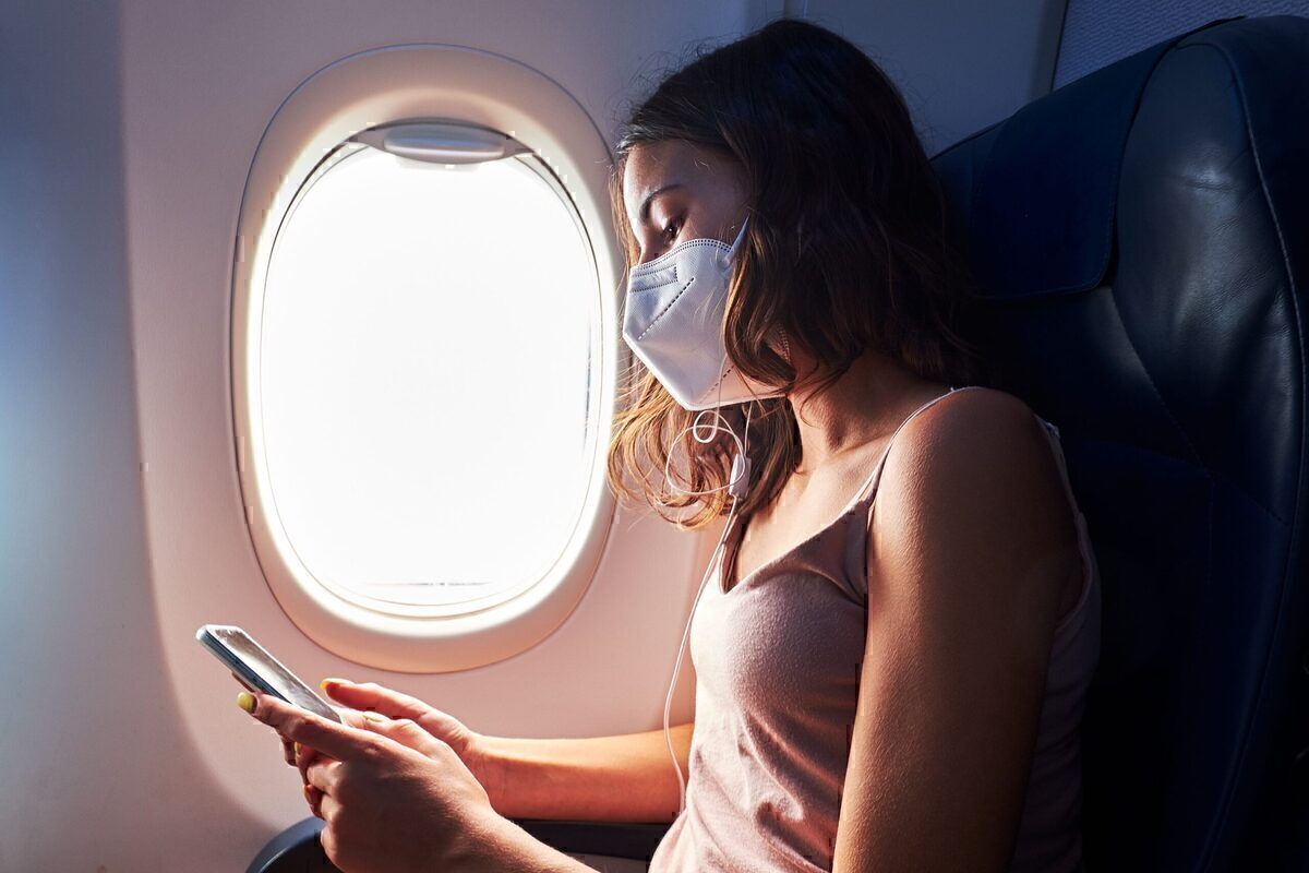 A Passenger using their mobile phone on an aircraft while wearing a face mask.