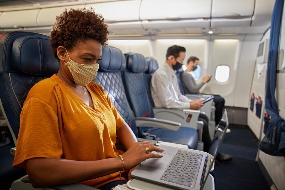 Masked customer in Comfort+ uses laptop inflight during COVID