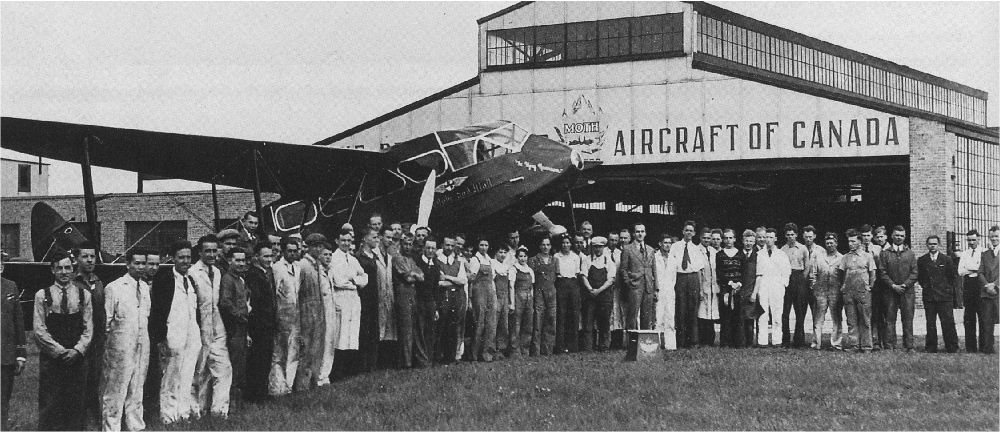 Dozens of workers near an aircraft parked outside a De Havilland Aircraft hangar.