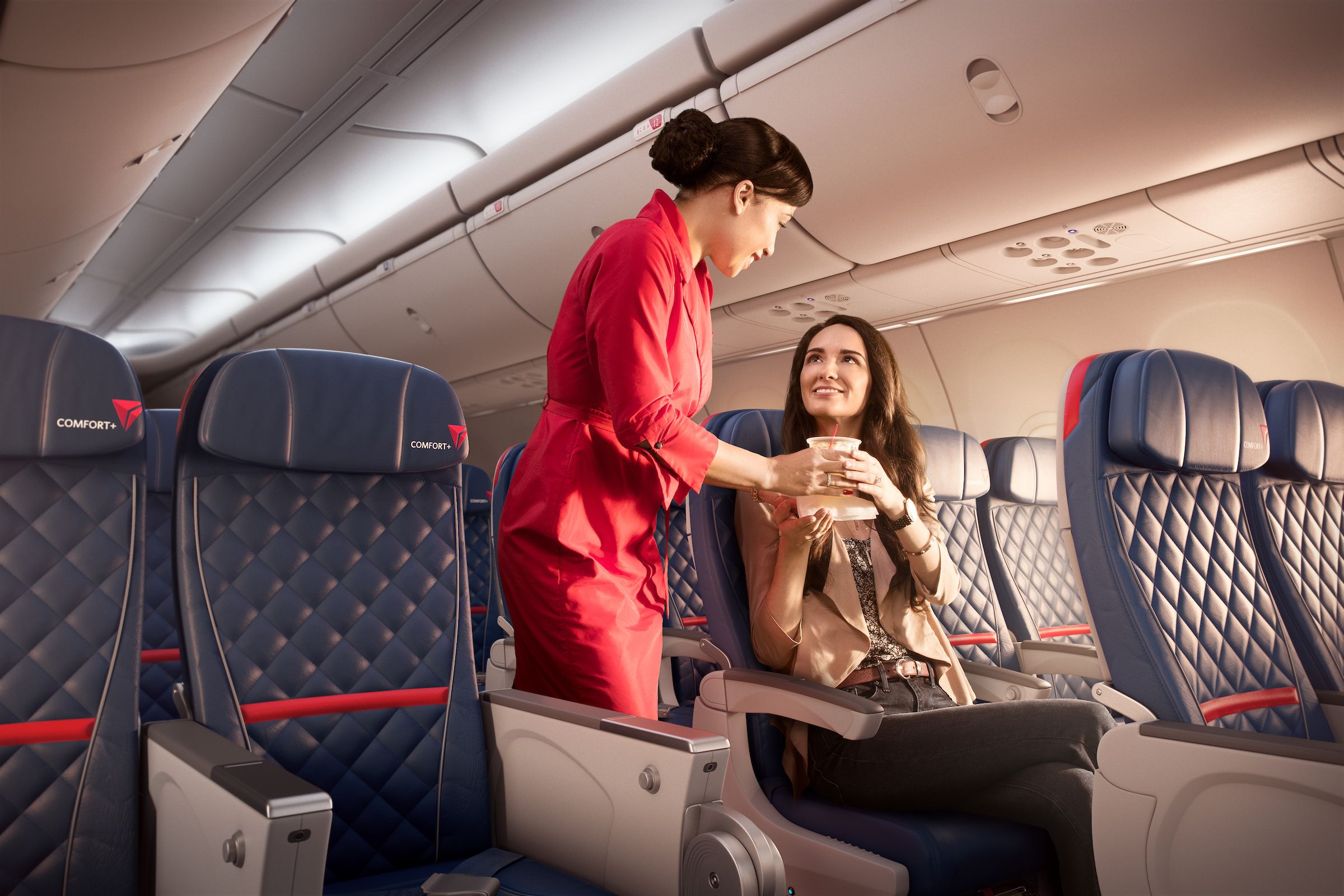 A Delta Air Lines flight attendant serving a passenger in a Delta Comfort+ seat.
