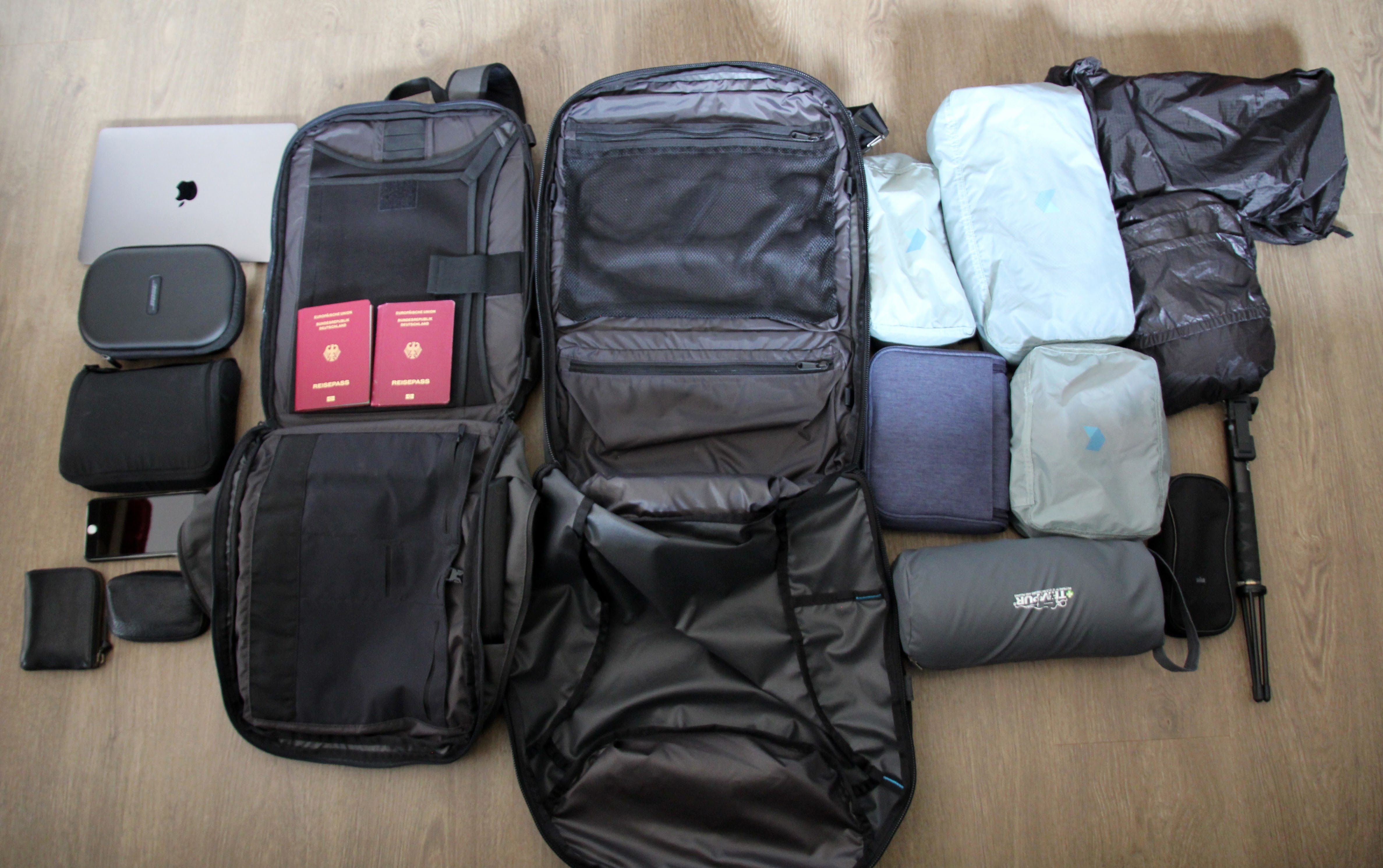 A travel backpack open with many smaller travel bags surrounding it.