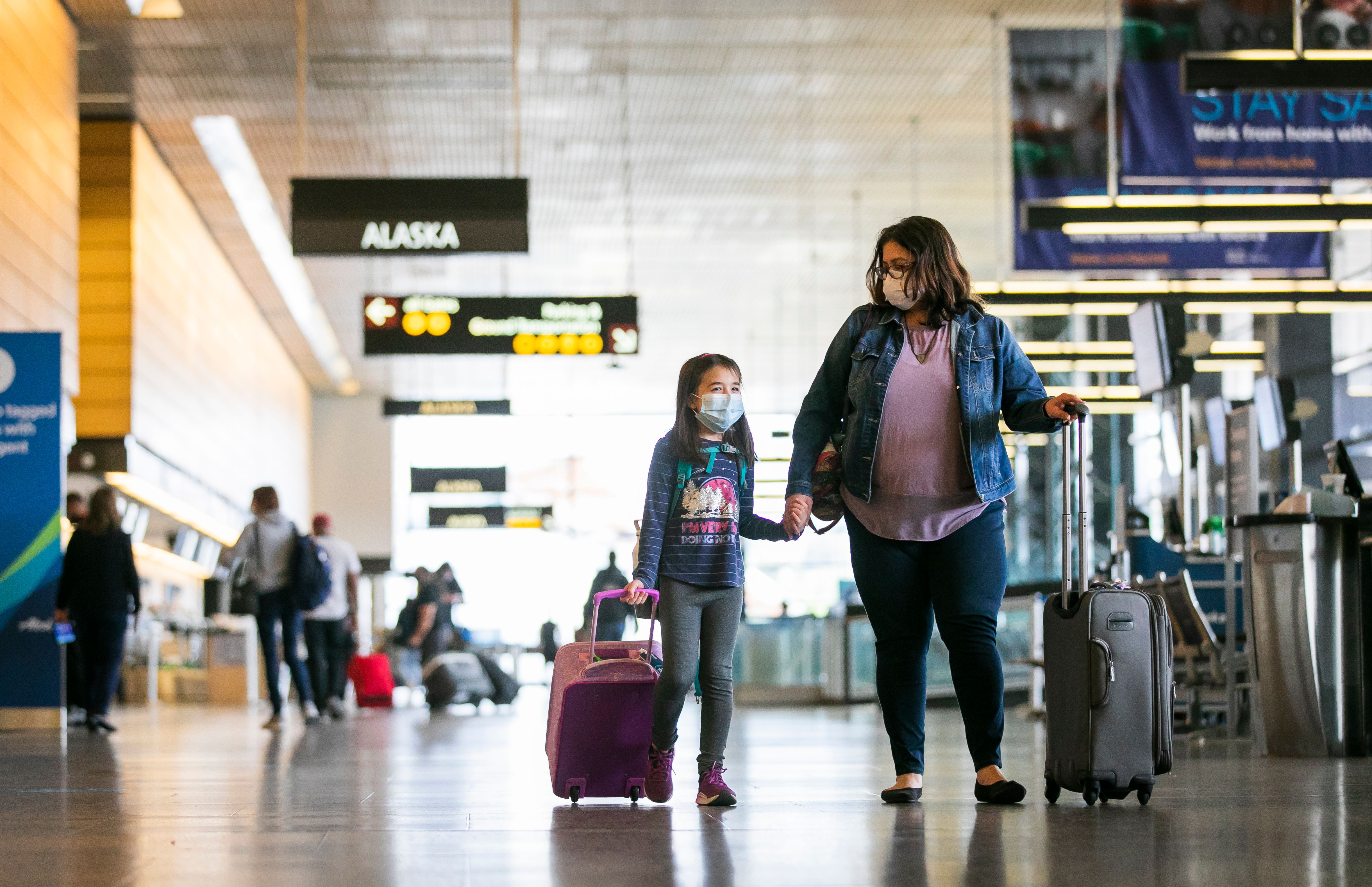 A mother and child walking with luggage in the terminal of SeaTac Airport.