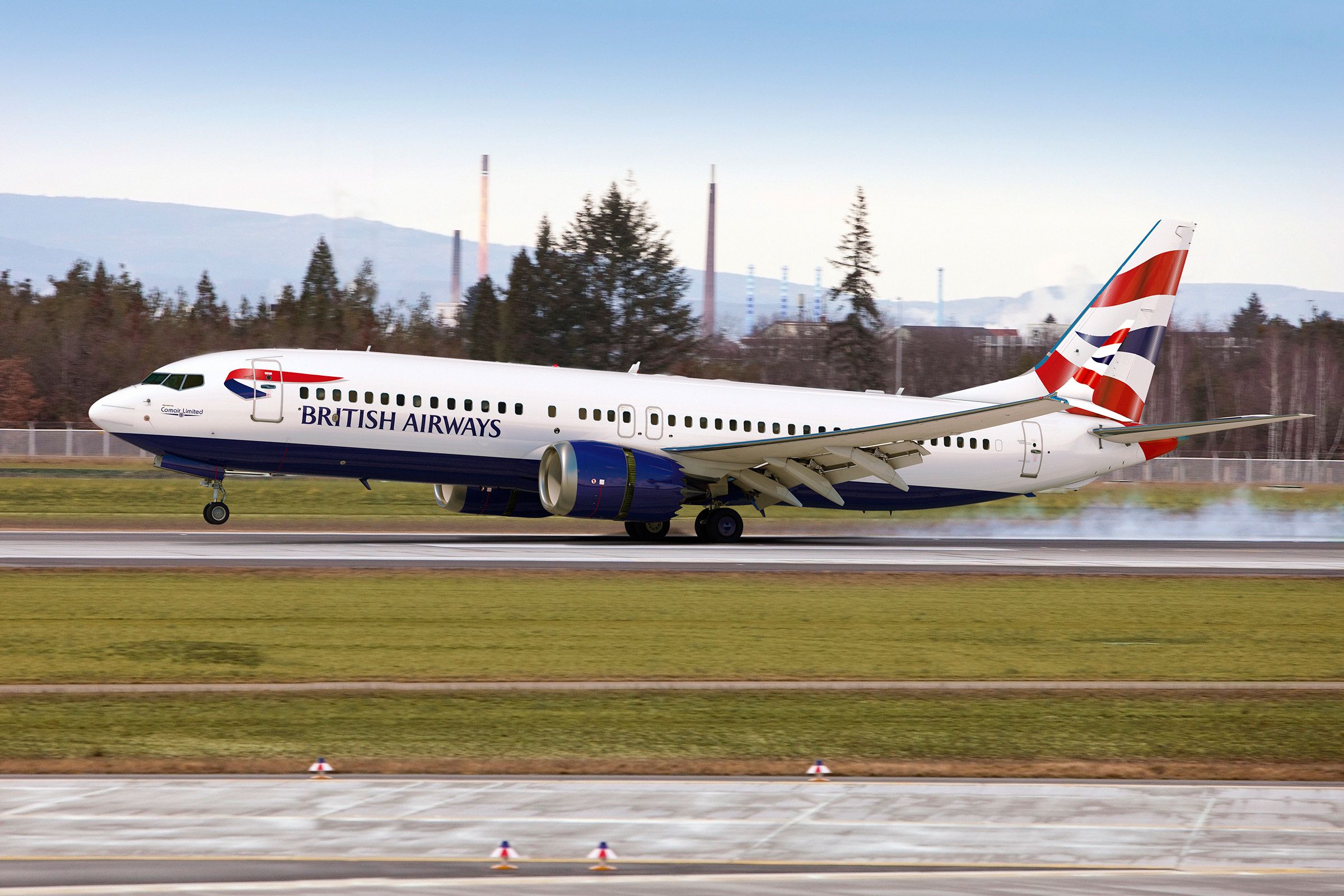 A Comair Boeing 737 MAX in the British Airways livery touches down with smoke generated by the wheels impacting the runway.