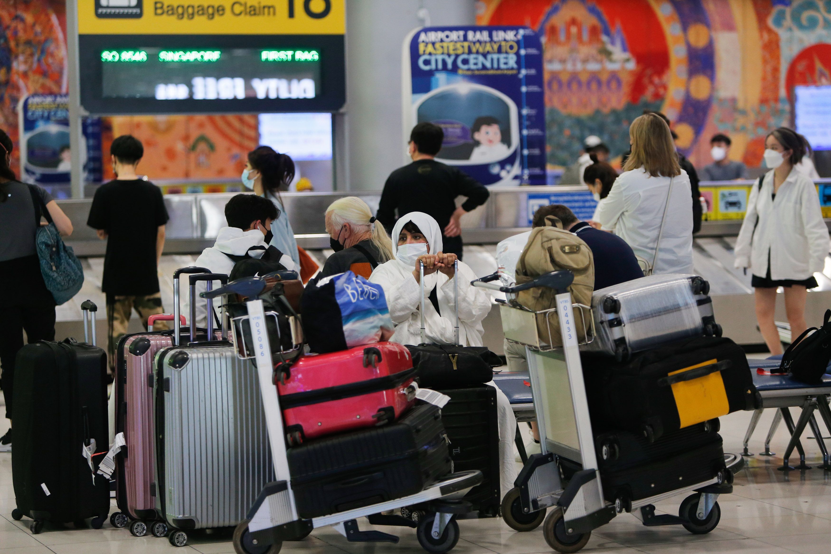 Traveler in face mask sitting in airport surrounded by luggage