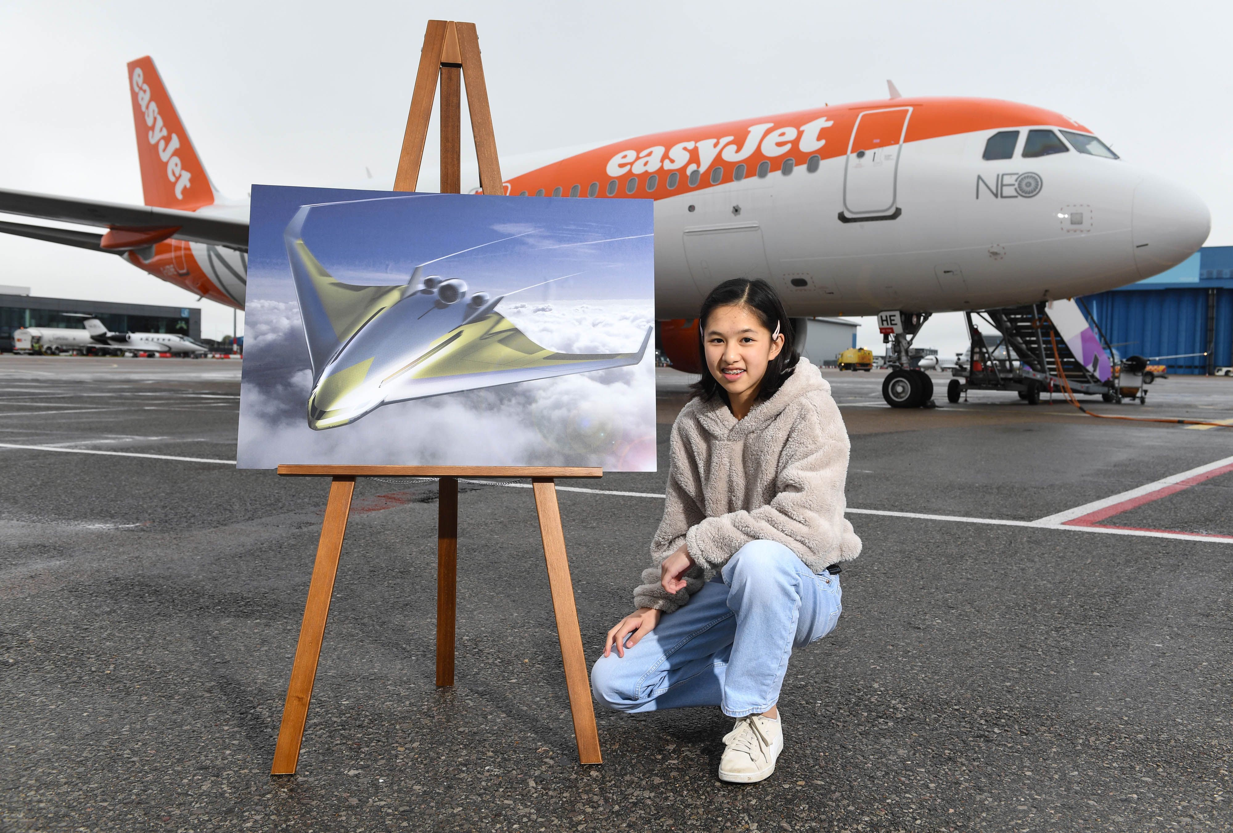 Girl standing in front of aircraft with rendering of new concept of zero emission blended wing aircraft