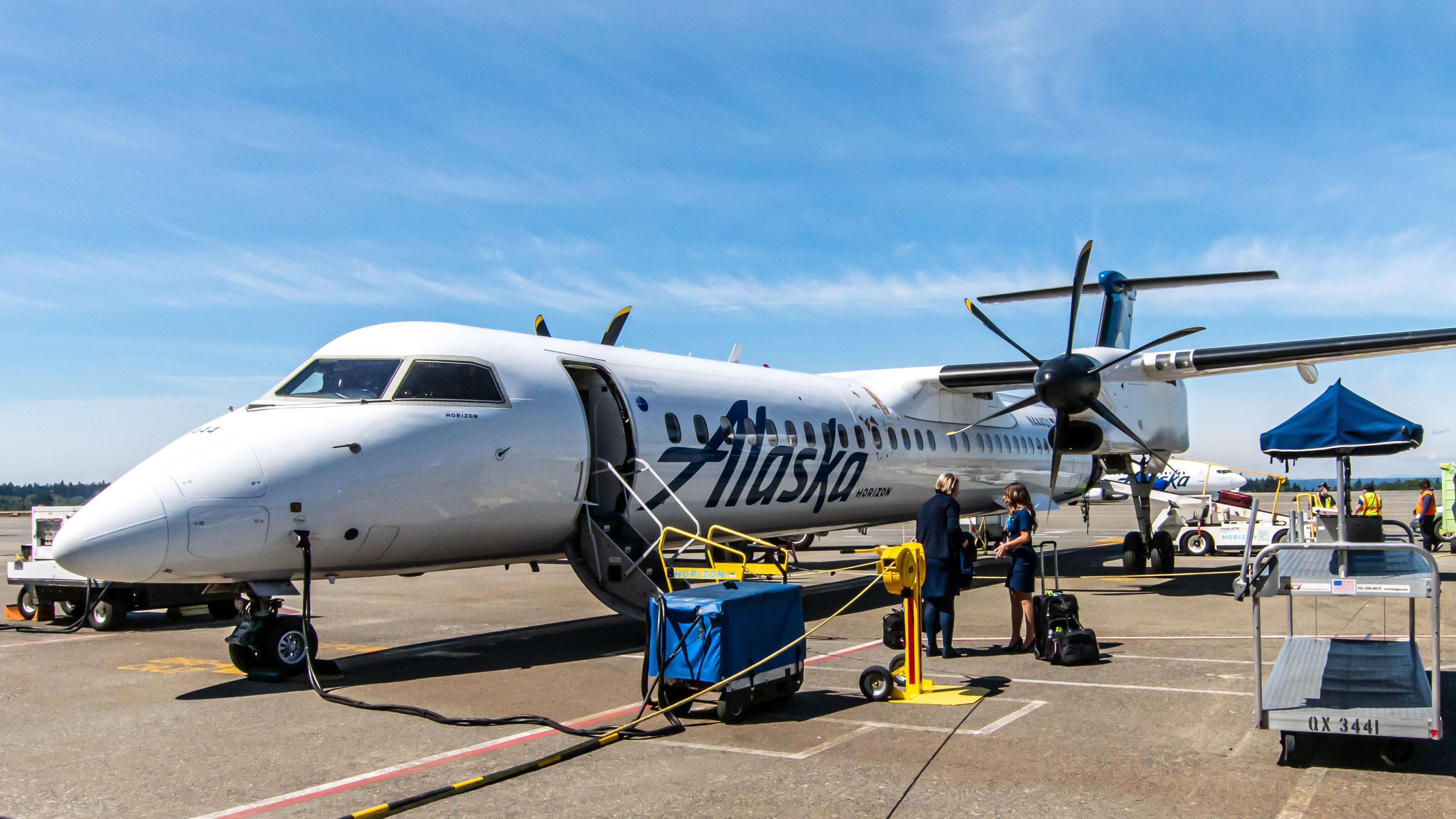 A Modern De Havilland Aircraft of Canada Dash 8 of Alaska Airlines at the SeaTac Gate in Friendly Skies with 2 Flight Attendants Briefing Each Other.  Note the A La Cart to the Right