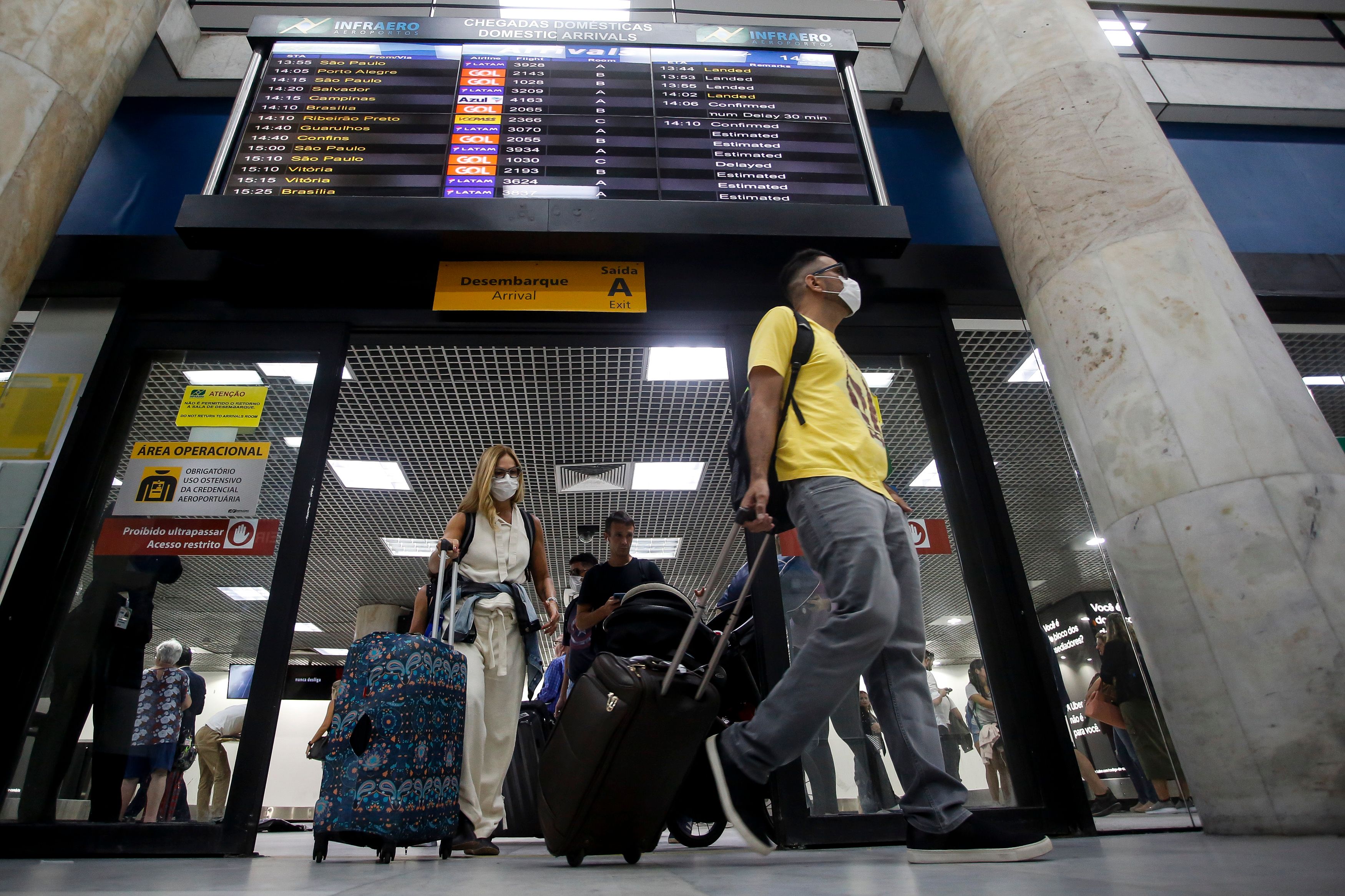 Passengers walk with their luggages wearing protective masks at Santos Dumont Airport in Rio de Janeiro, Brazil.