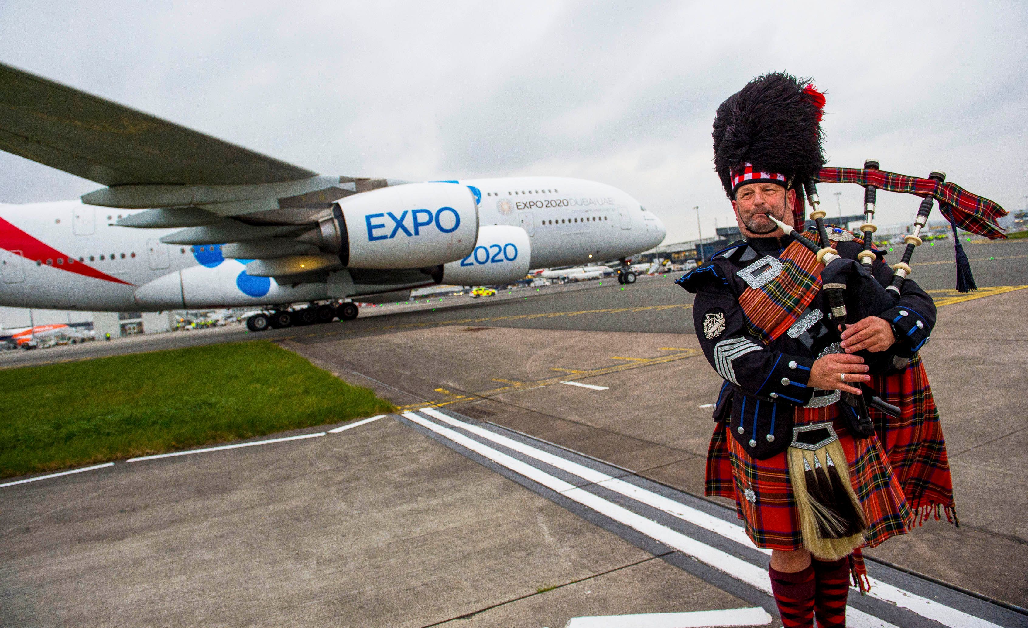A380 at Glasgow Airport with man playing bagpipes in national dress 