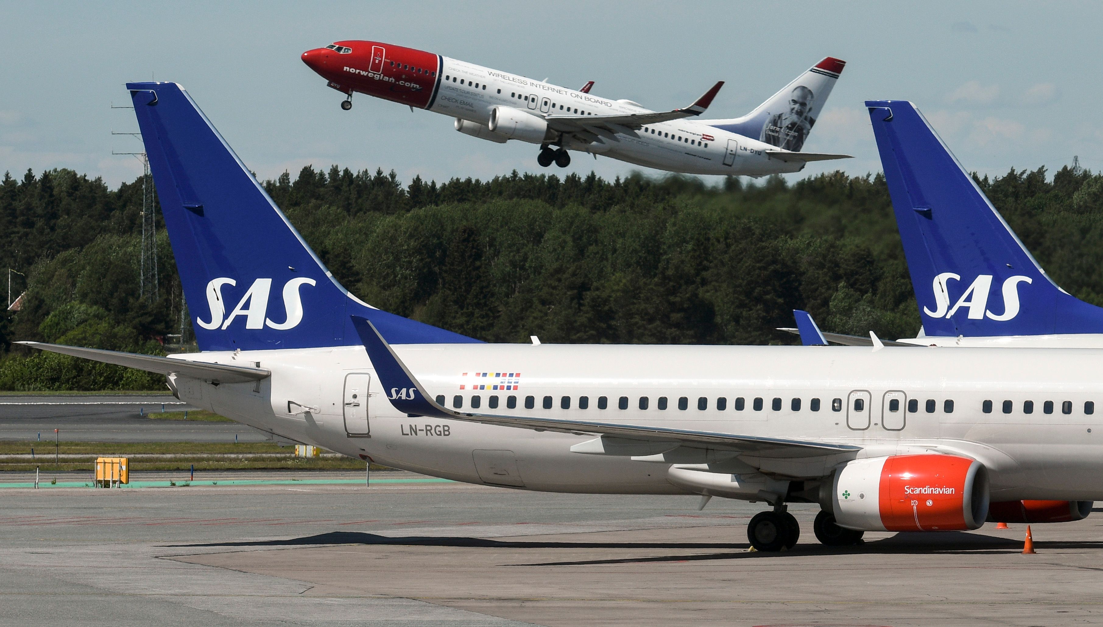 Norwegian plane taking off from Stockholm airport with SAS planes in the foreground