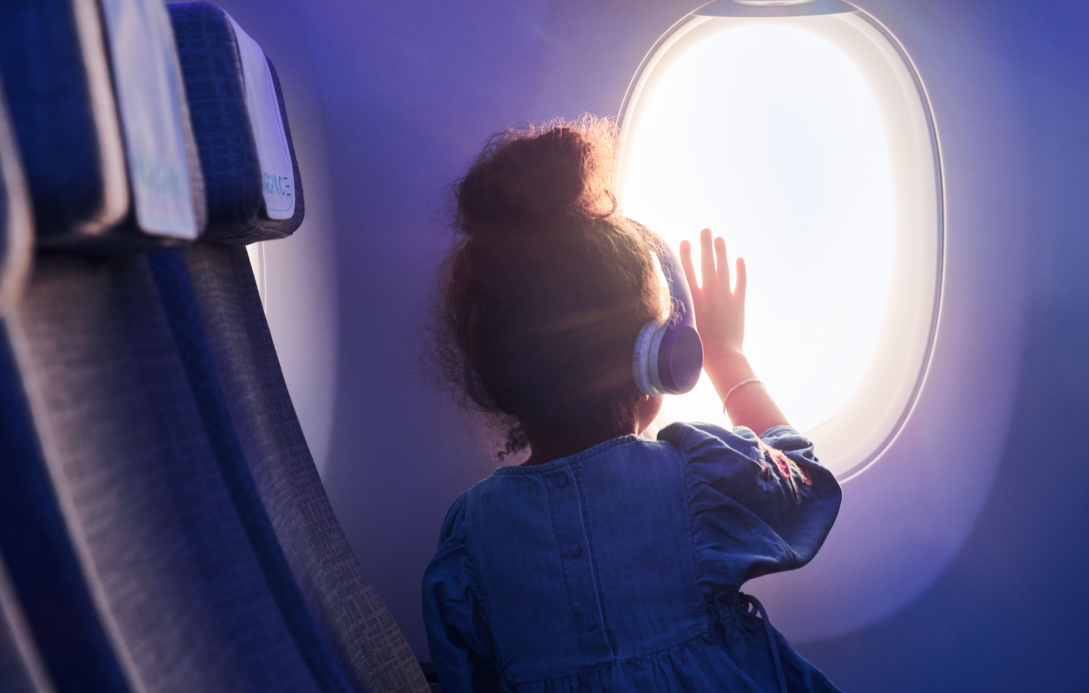 A child looking out an aircraft window wearing headphones.