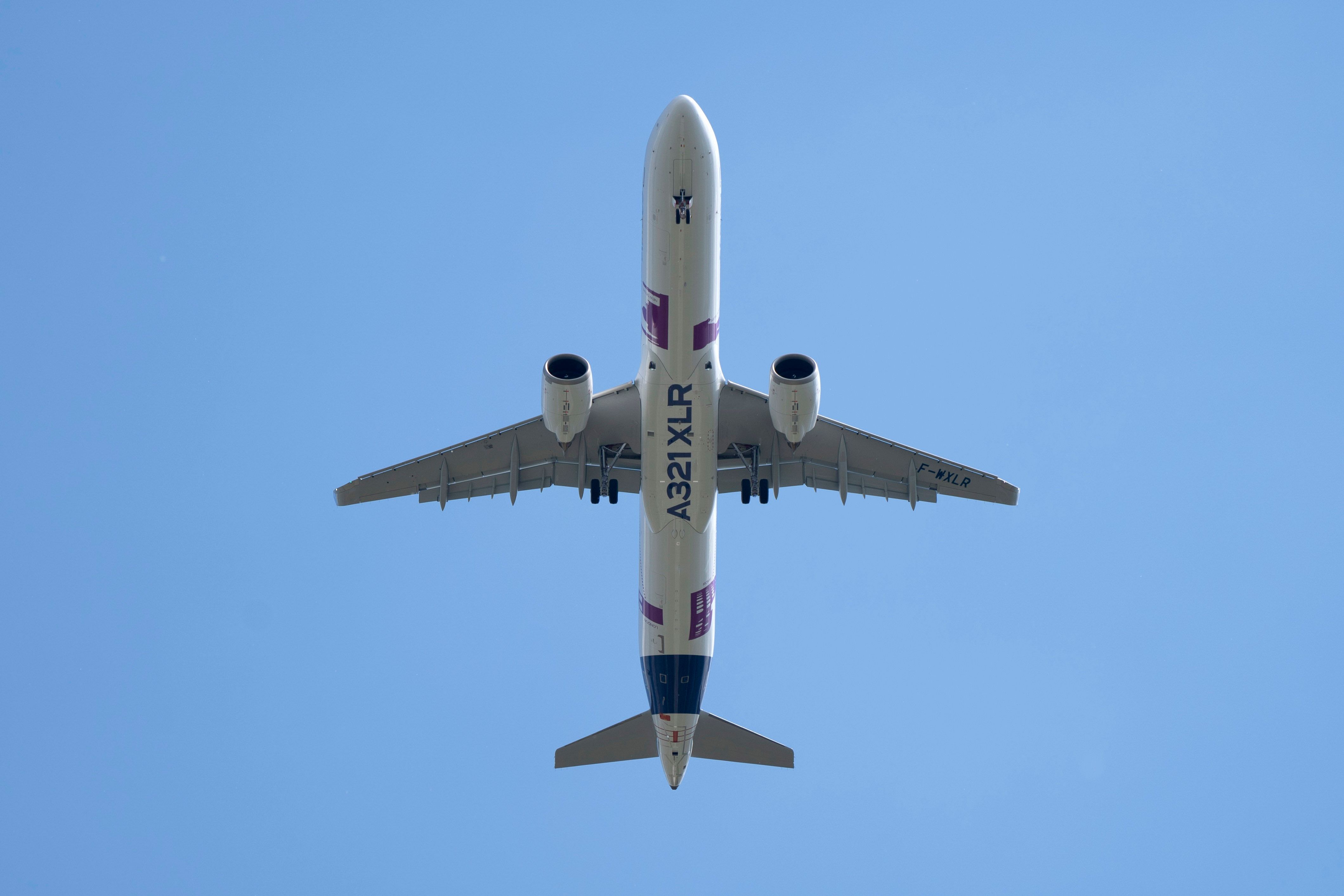 View from the ground looking up at an Airbus A321XLR flying overhead.