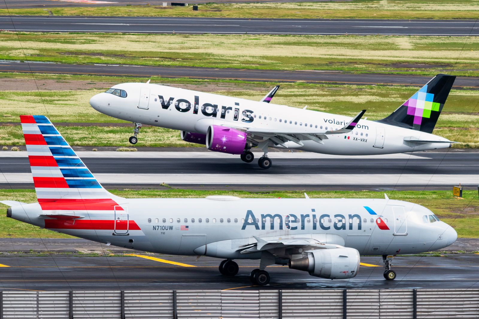 An American Airlines Airbus A319 in the front and a Volaris aircraft departing in the back in Mexico City. 