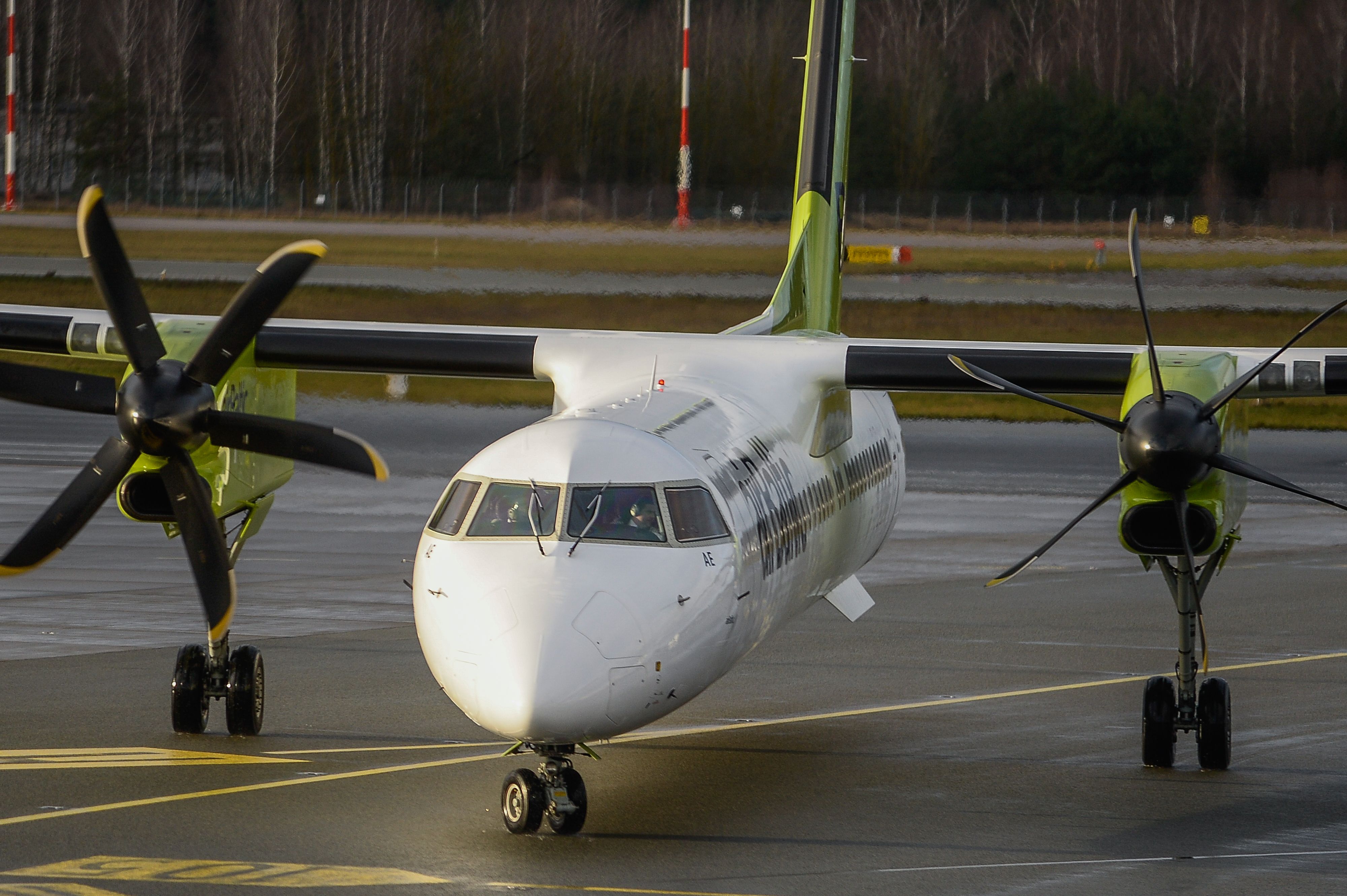 An airBaltic Q400 moving towards its assigned gate on one engine