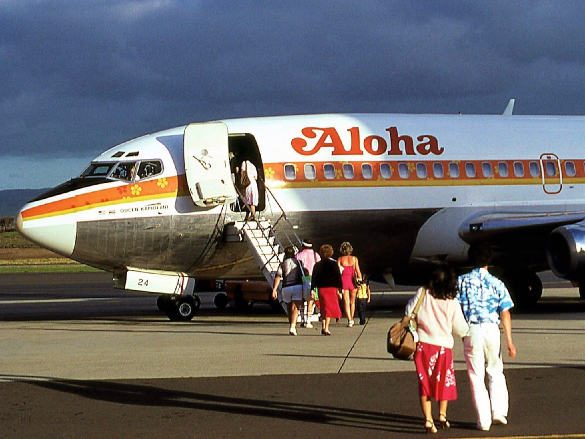 Several passengers boarding an Aloha Airlines aircraft from the airport apron.