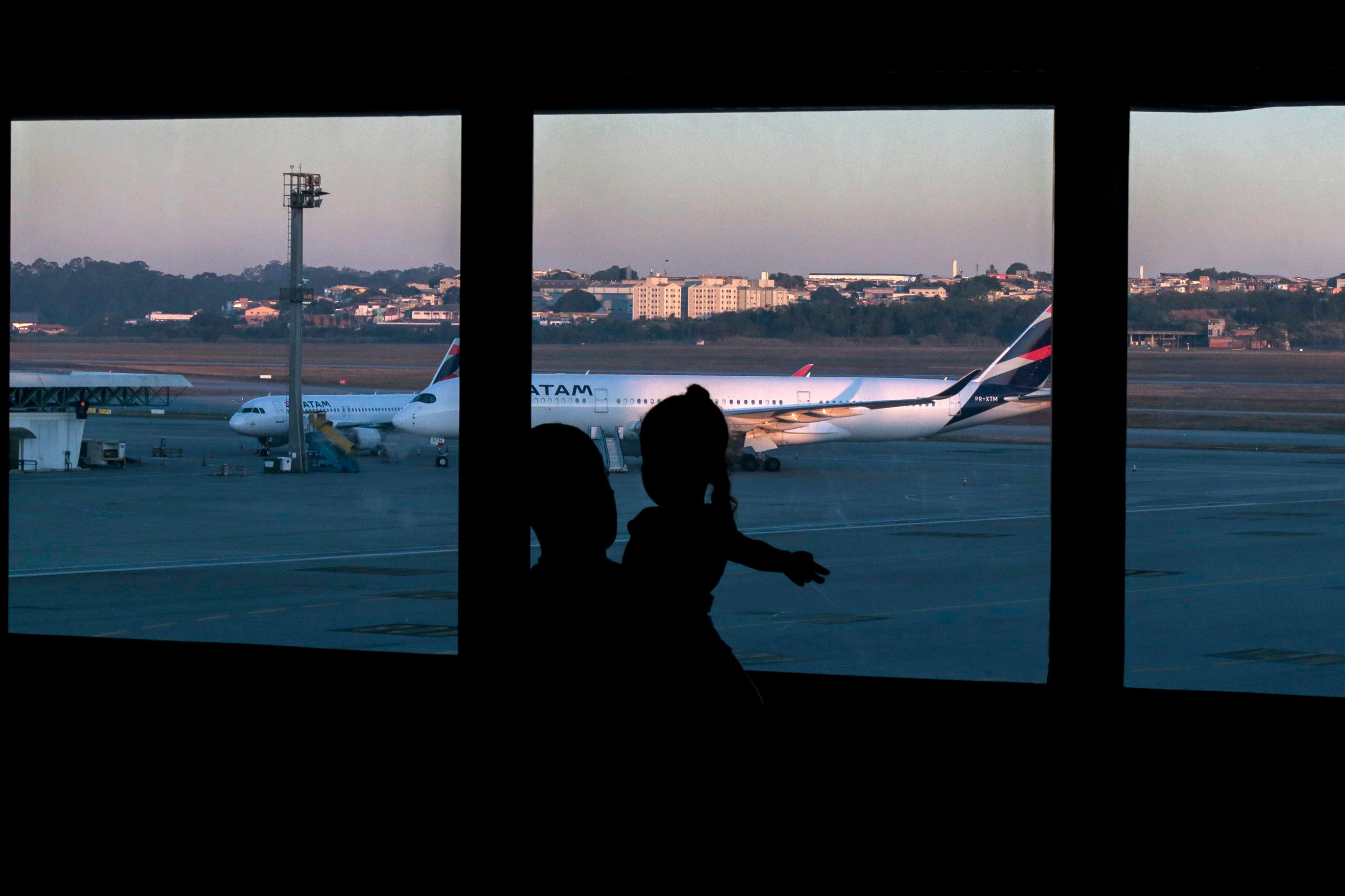 A Colombian citizen and a girl look at planes sitting at the tarmac of Guarulhos International Airport, in Guarulhos, near Sao Paulo, Brazil, on May 26, 2020.