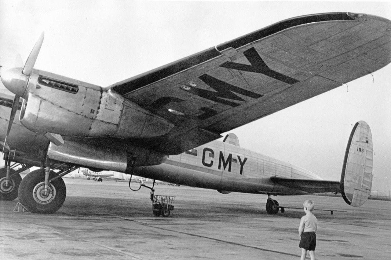 A Young boy watching a Lancasterian aircraft parked on an airport apron.