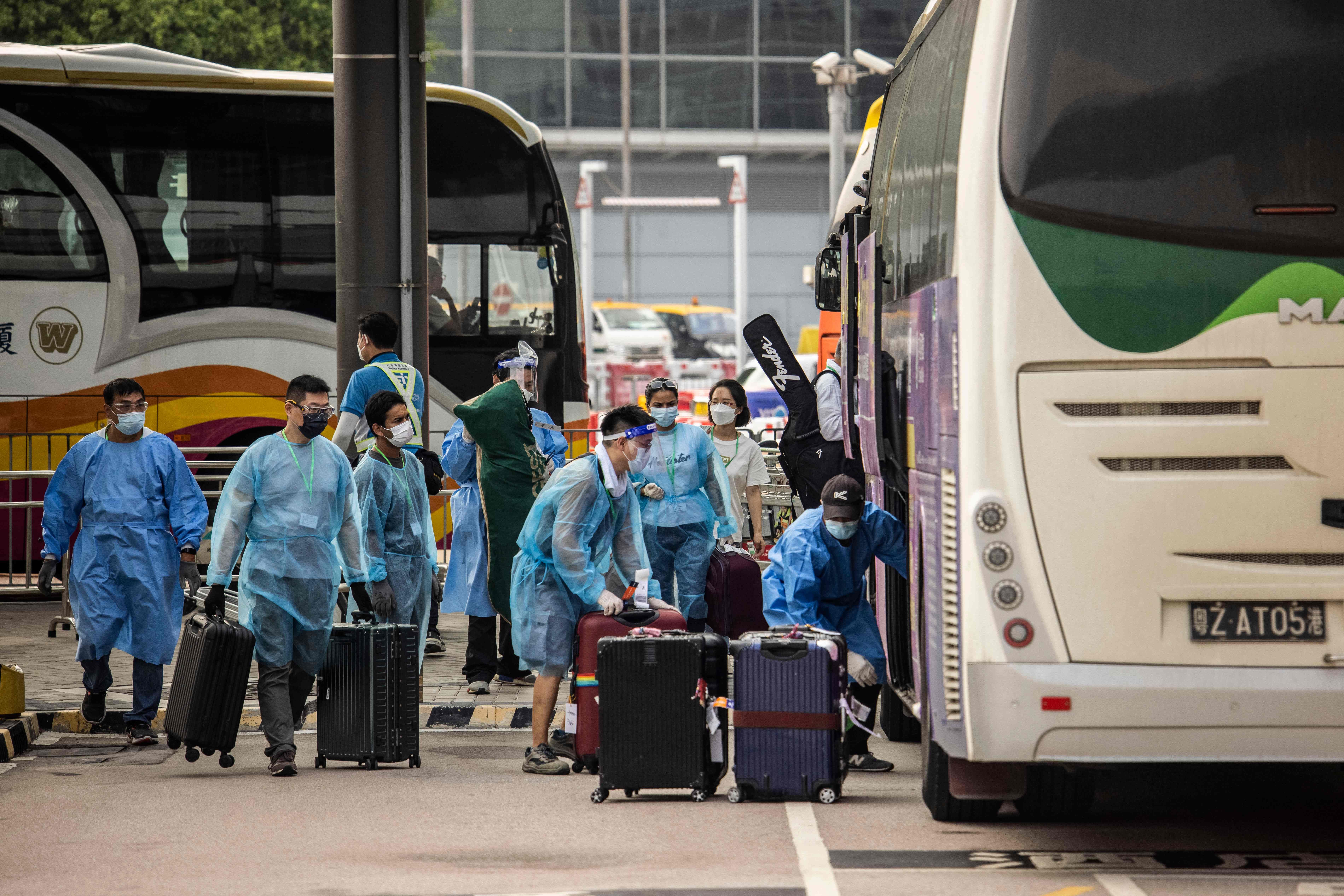 Workers load traveller's luggage onto a bus at Hong Kong International Airport before taking them to hotel quarantine on September 23, 2022. - Hong Kong announced on September 23 it will end mandatory hotel quarantine, scrapping some of the world's toughest travel restrictions that have battered the economy and kept the finance hub internationally isolated.