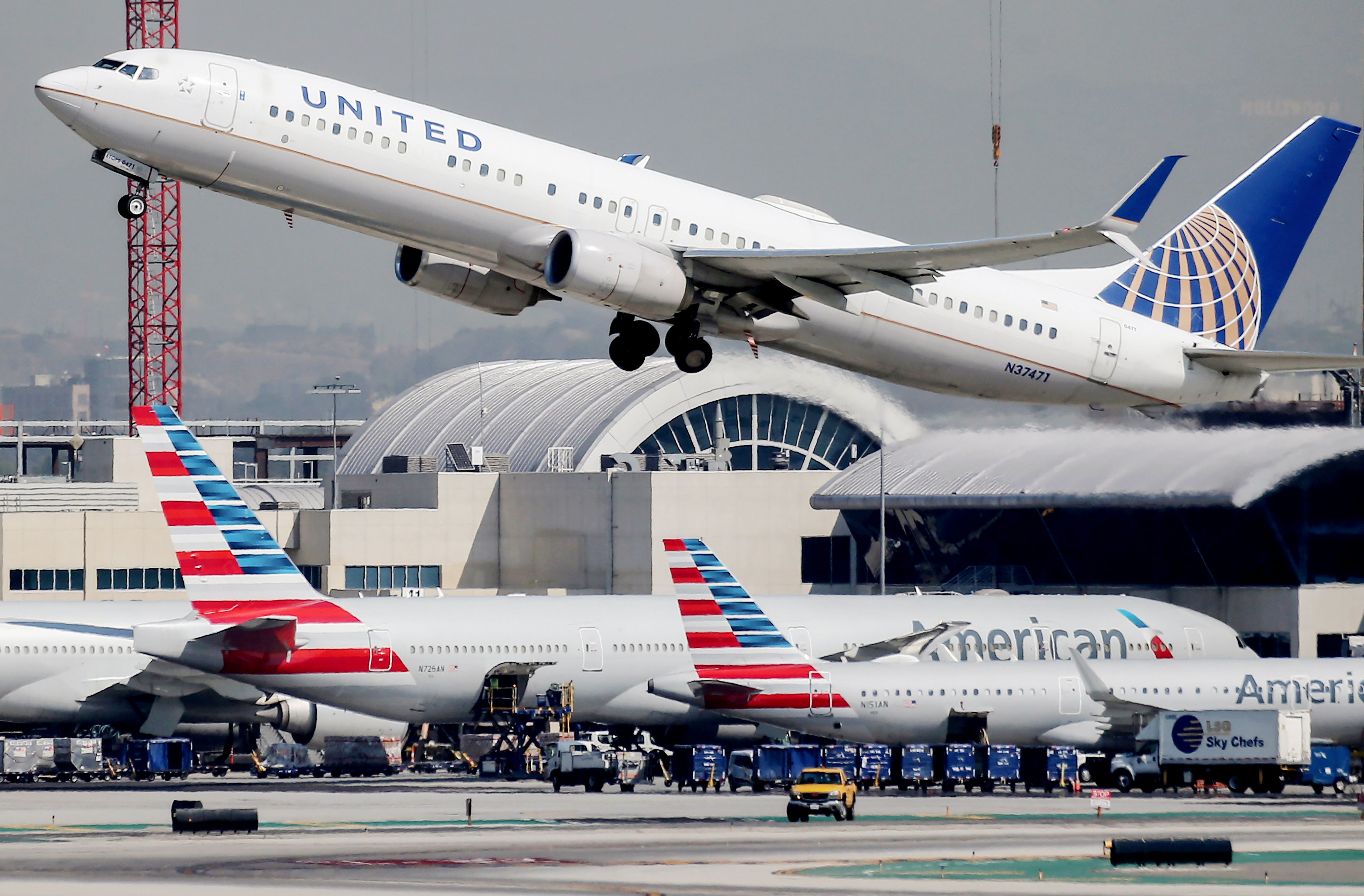 A United Airlines plane takes off above American Airlines planes