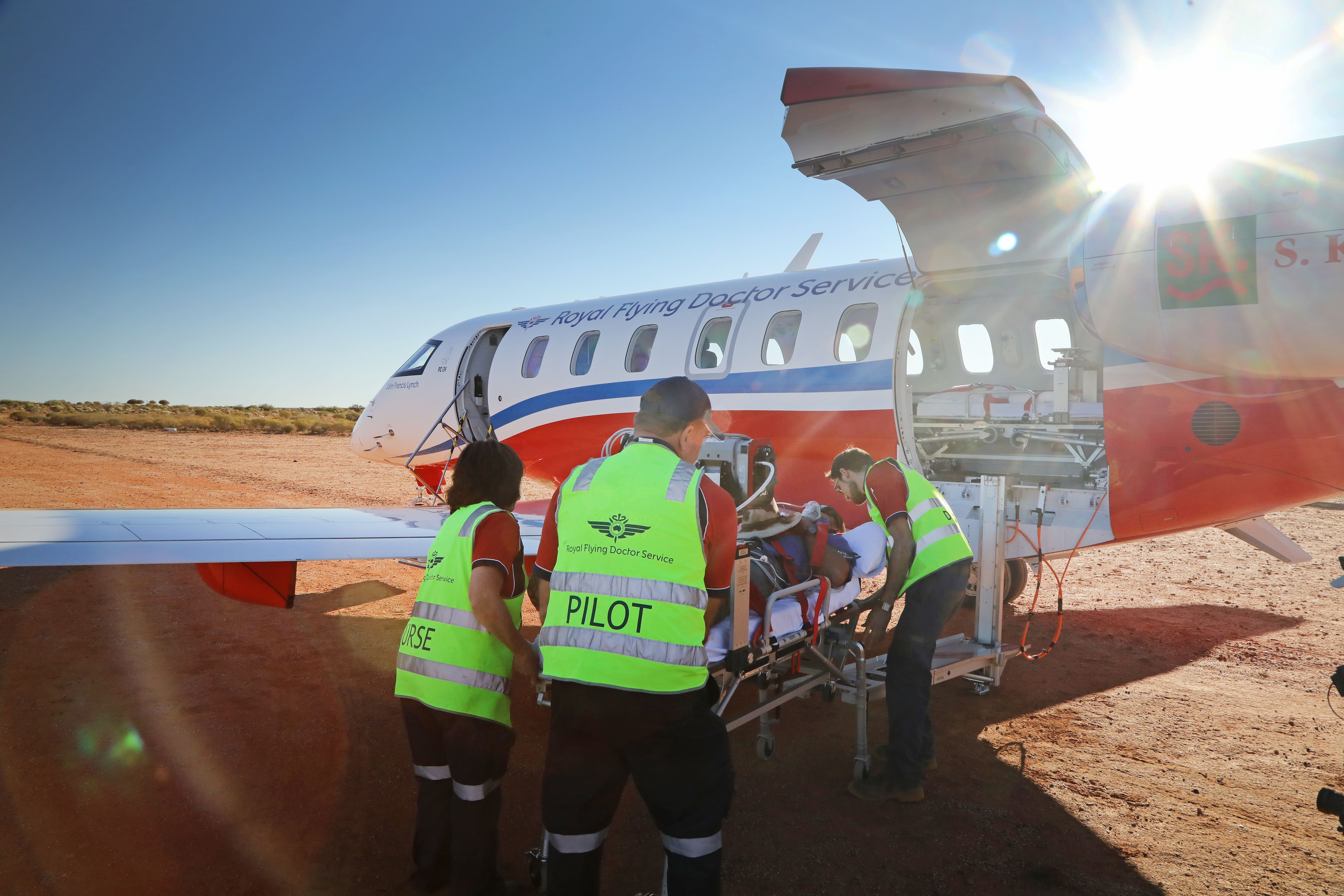 A nurse, doctor, and pilot help a sick patient on a stretcher board a Royal Flying Doctor Medevac aircraft.
