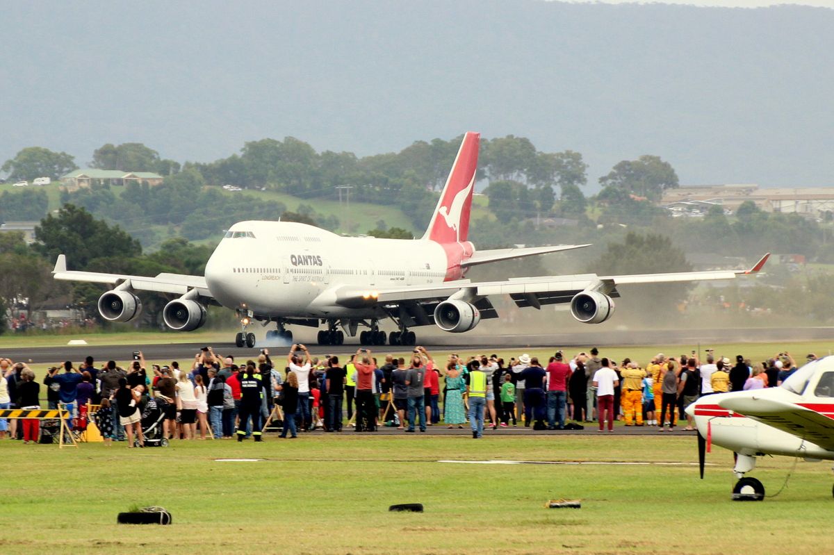 A Qantas Boeing 747 landing on a runway amidst a crowd of spectators.