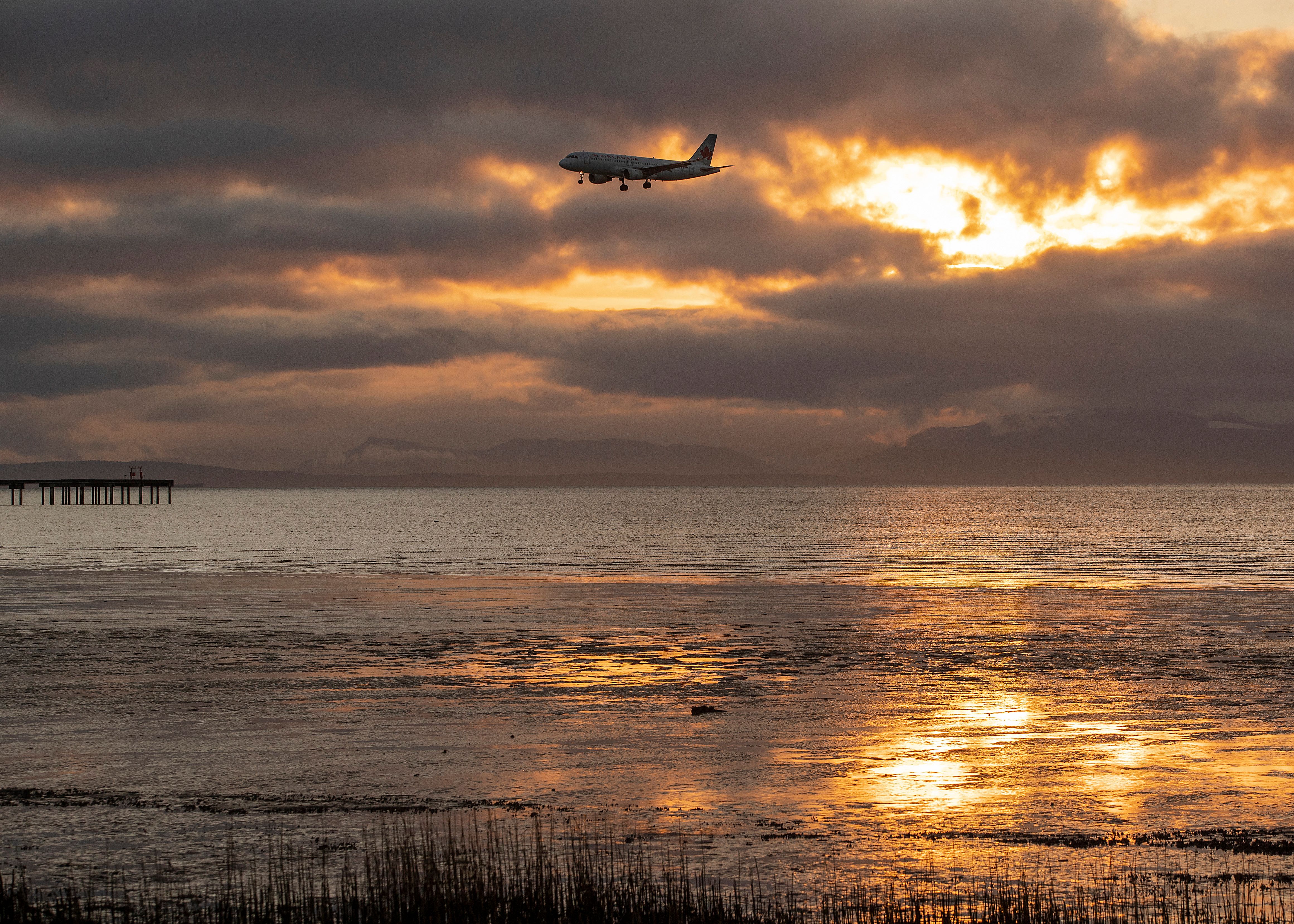 Air Canada plane coming in for landing over landscape at sunset