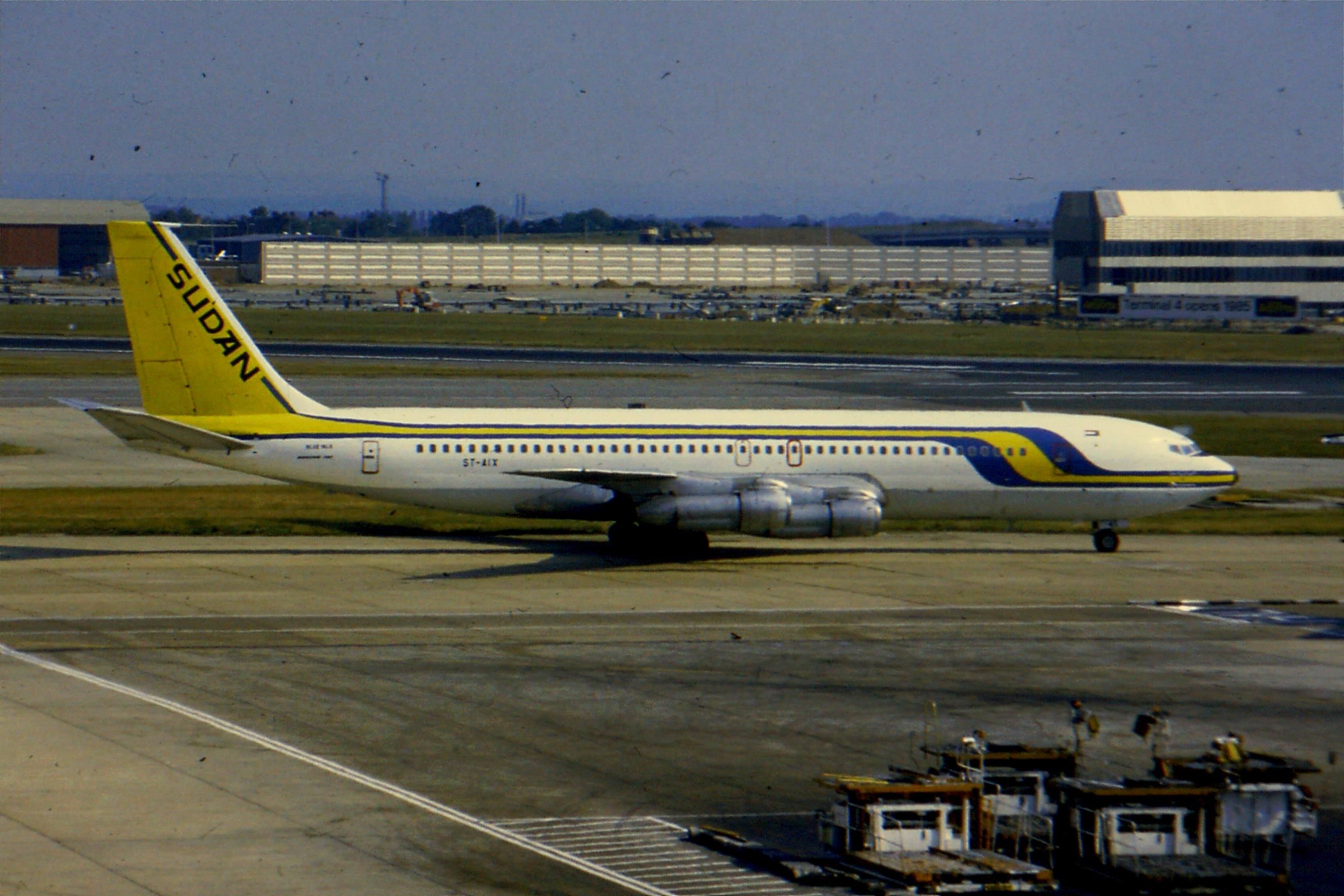 A white jetliner with a yellow tail and Sudan Airways branding in blue parked at an airport