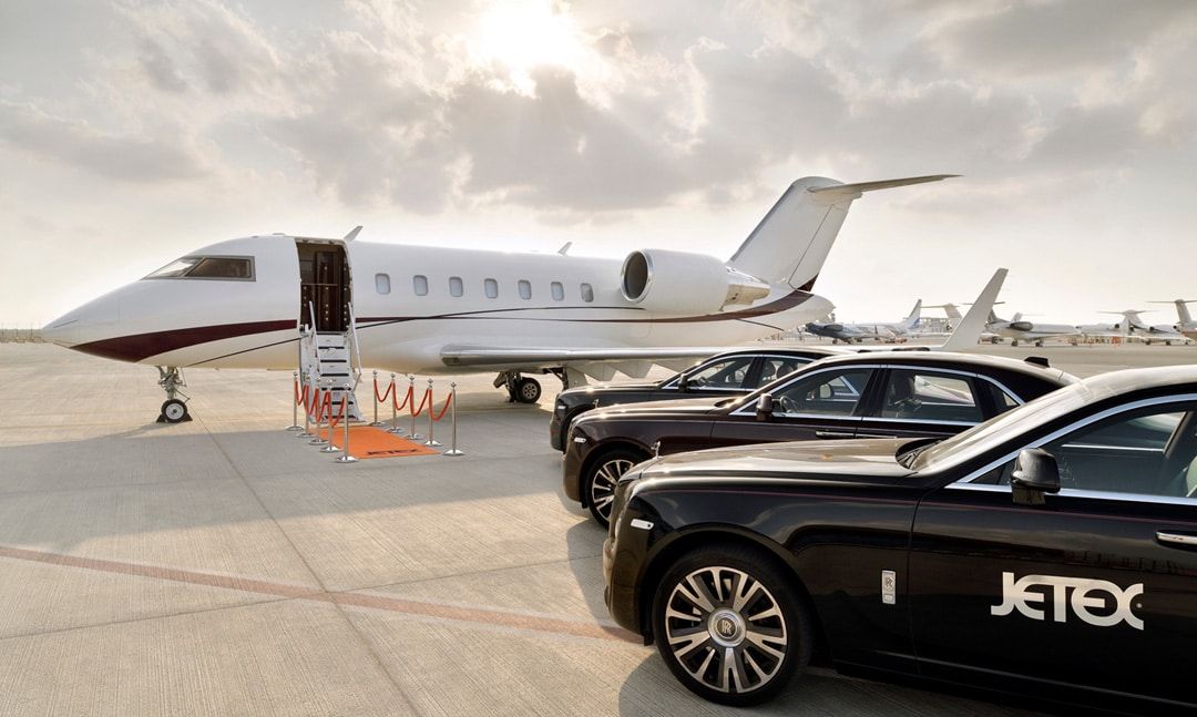 Multiple luxury vehicles parked next to a Private Jet.