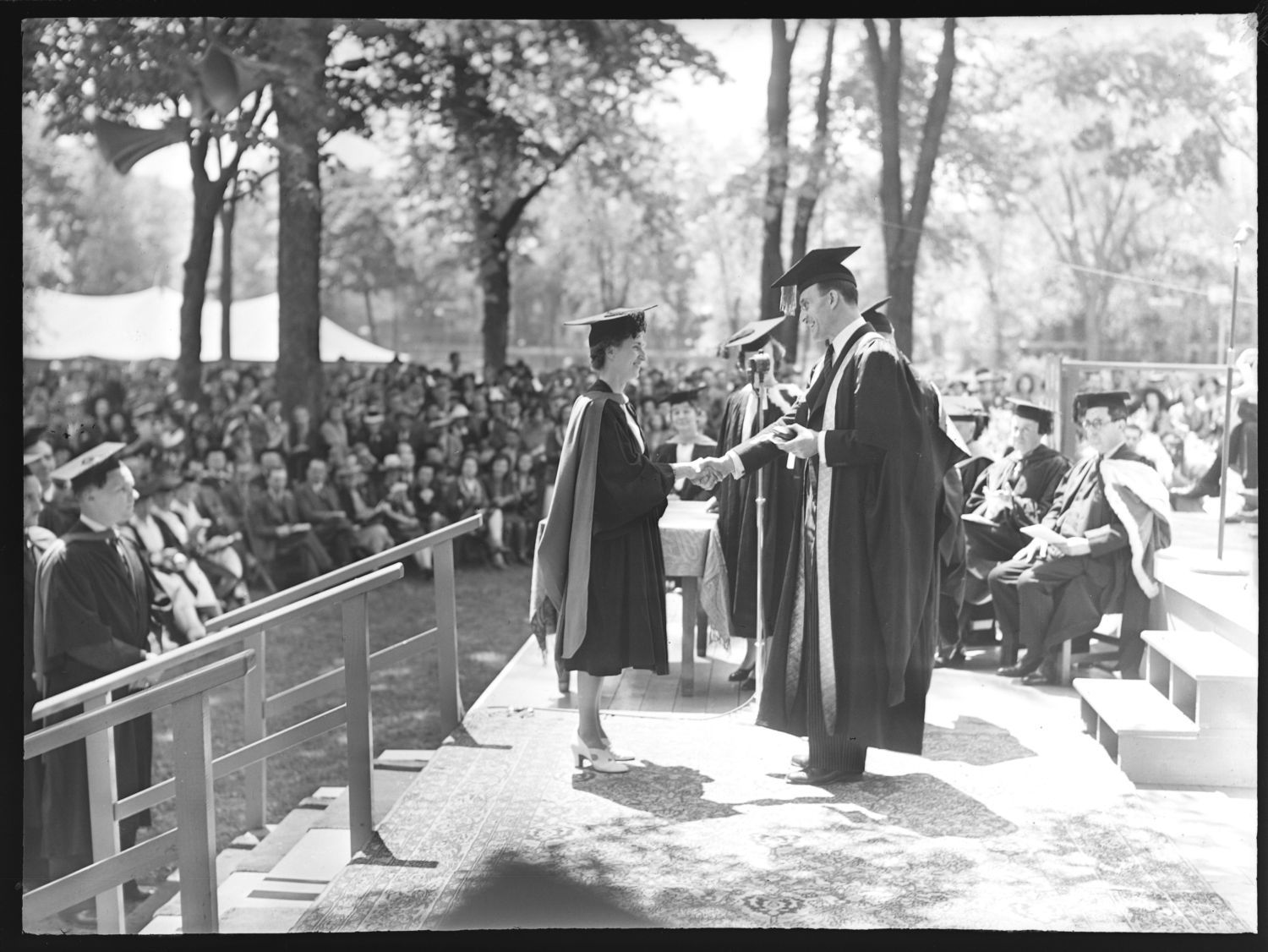 A woman in a cap and gown for graduation shaking hands with a university official