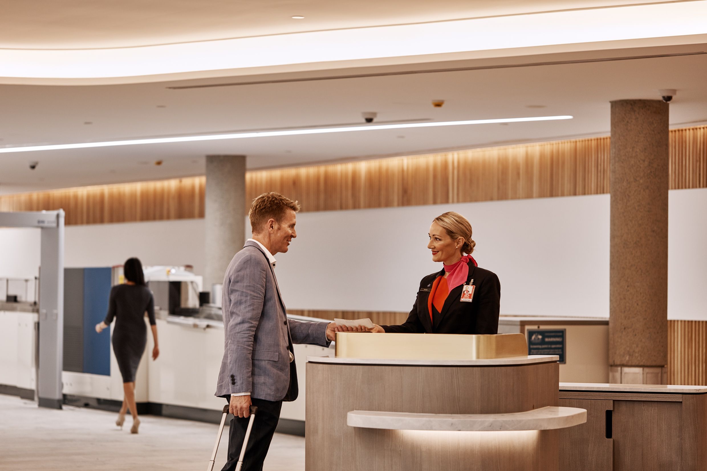 Un homme avec une valise roulante remet une carte d'embarquement au préposé à l'enregistrement travaillant au comptoir Qantas