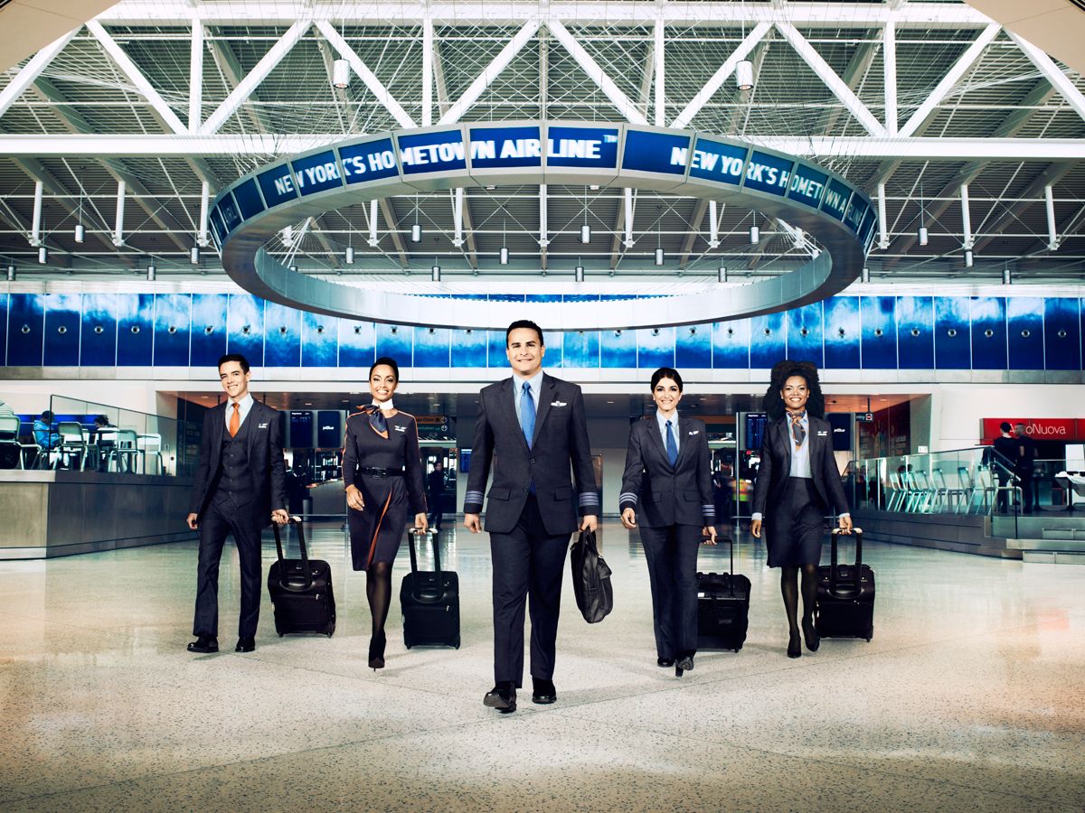 Several JetBlue flight attendants with bags waling in an airport terminal.