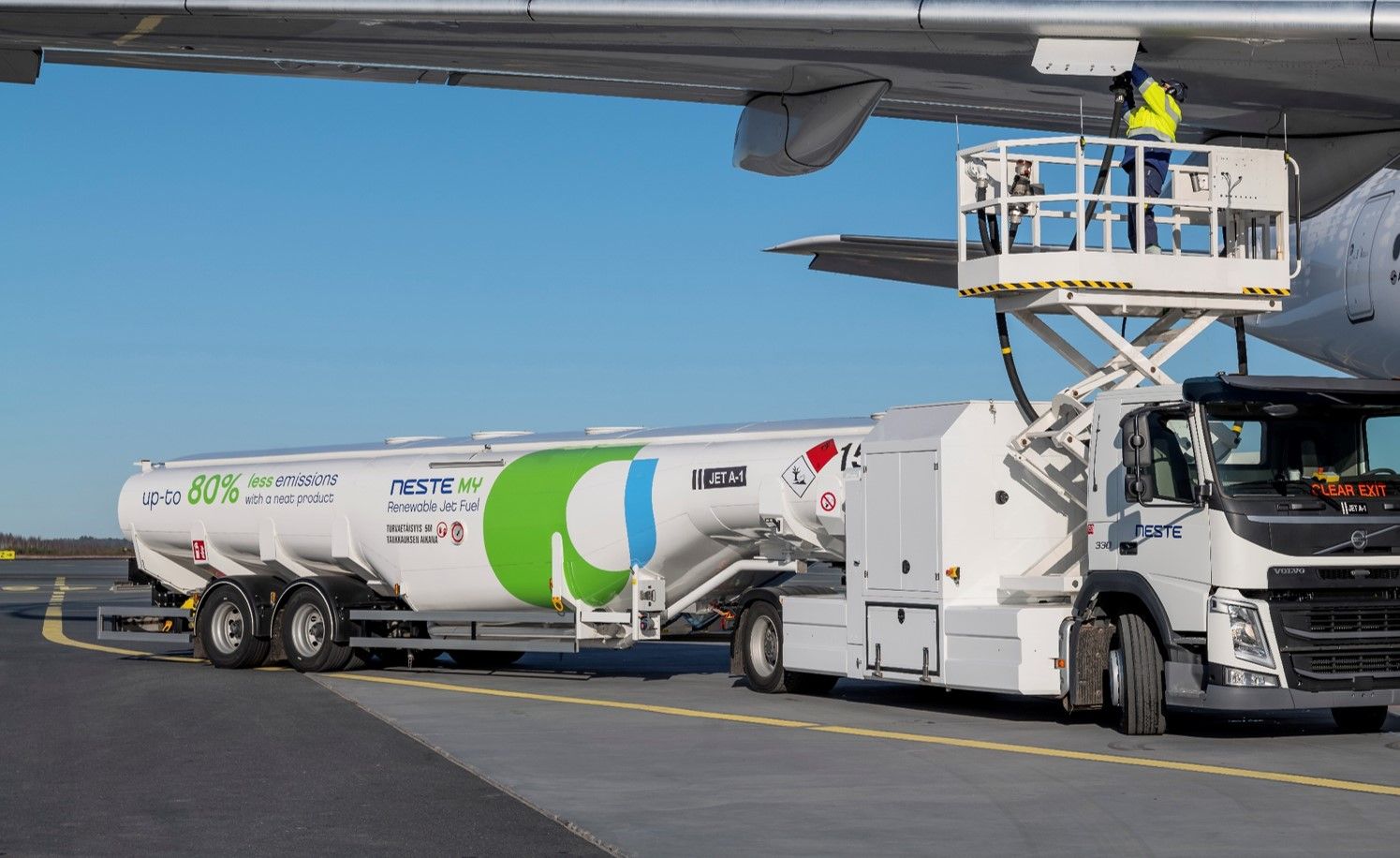 A Neste truck filled with sustainable aviation fuel parked beneath an aircraft wing.