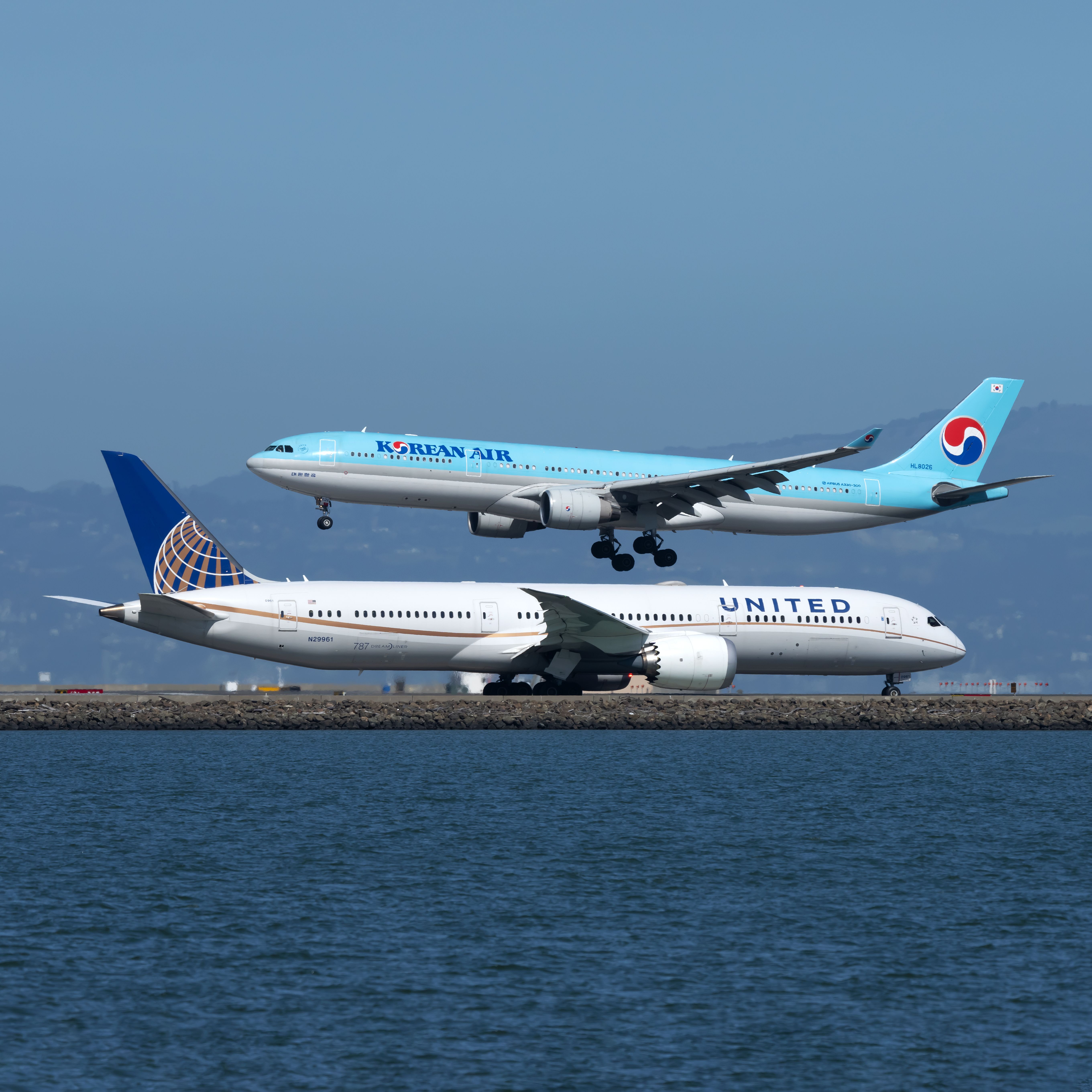 A United Airlines Boeing 787-9 Dreamliner on an airport apron, as a Korean Air aircraft lands.