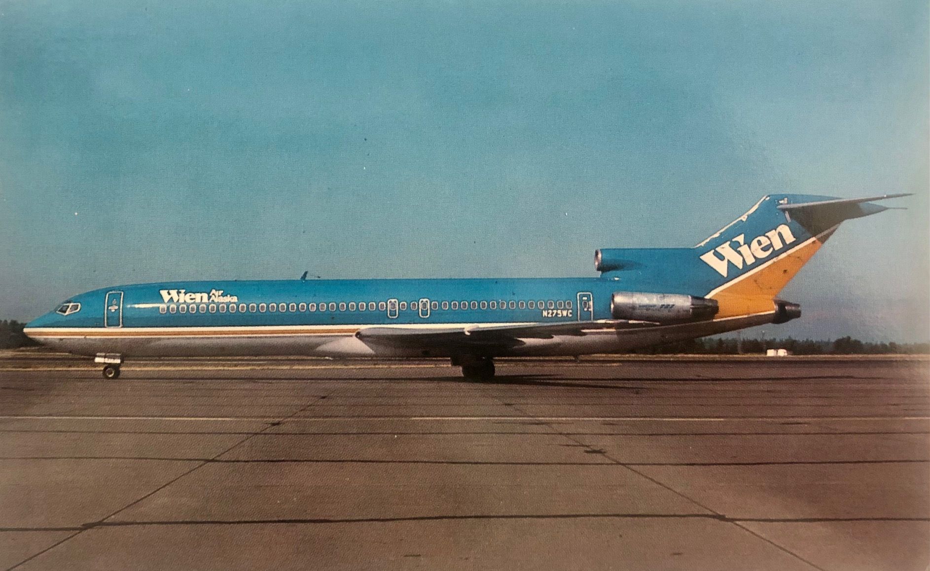 A blue Boeing 737 aircraft with white Wien Air Alaska lettering sits on a runway