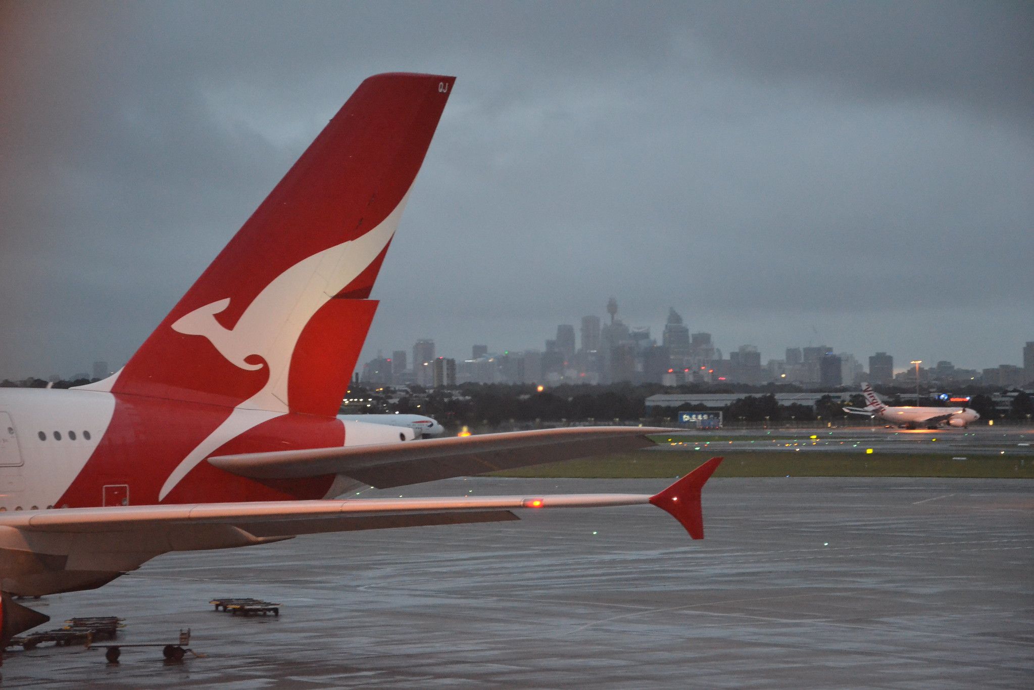 Sydney Airport in the rain - A380 tail and winglet of Qantas in front of Sydney skyline in overcast