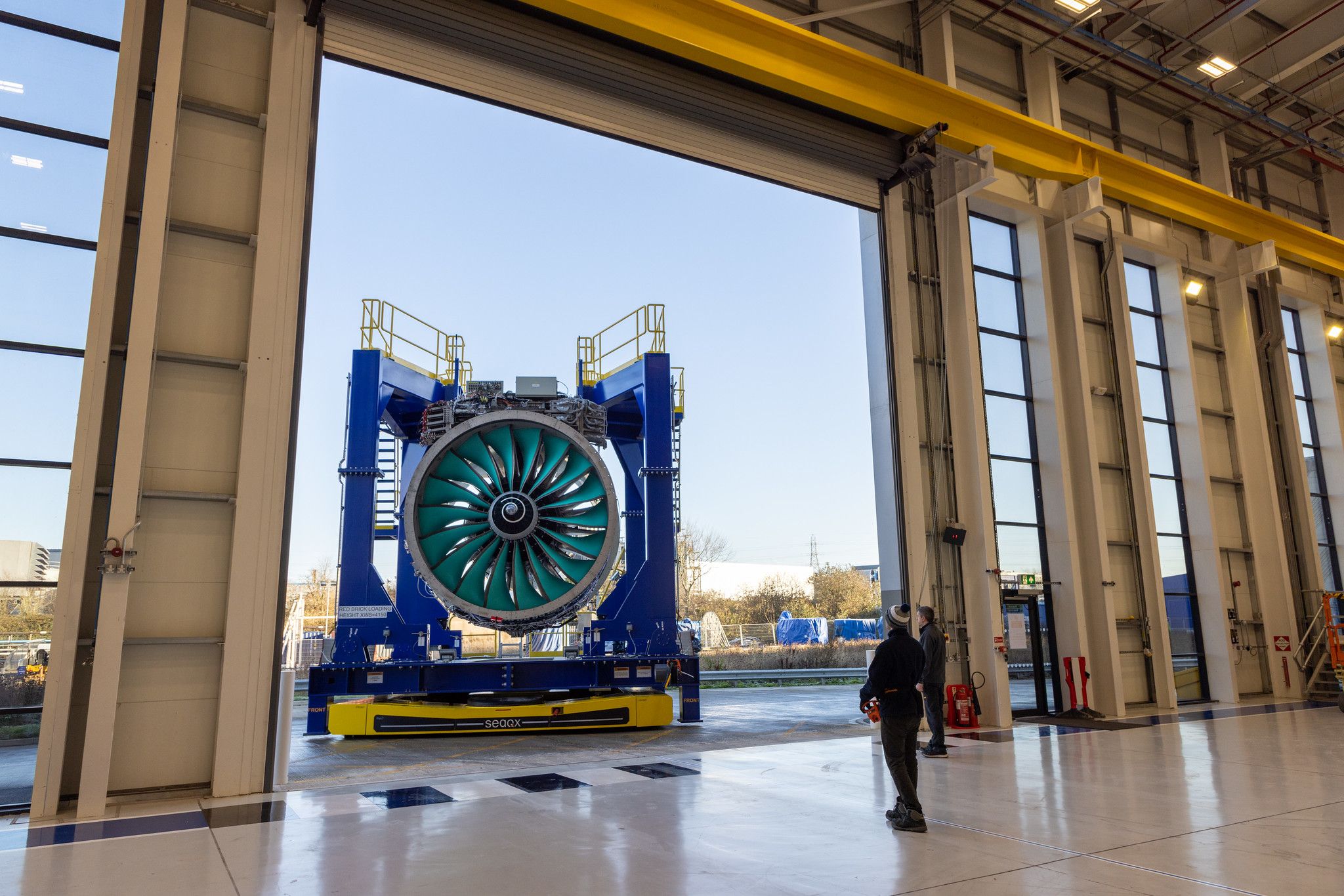 A Rolls Royce engine being moved outside of a maintenance facility.