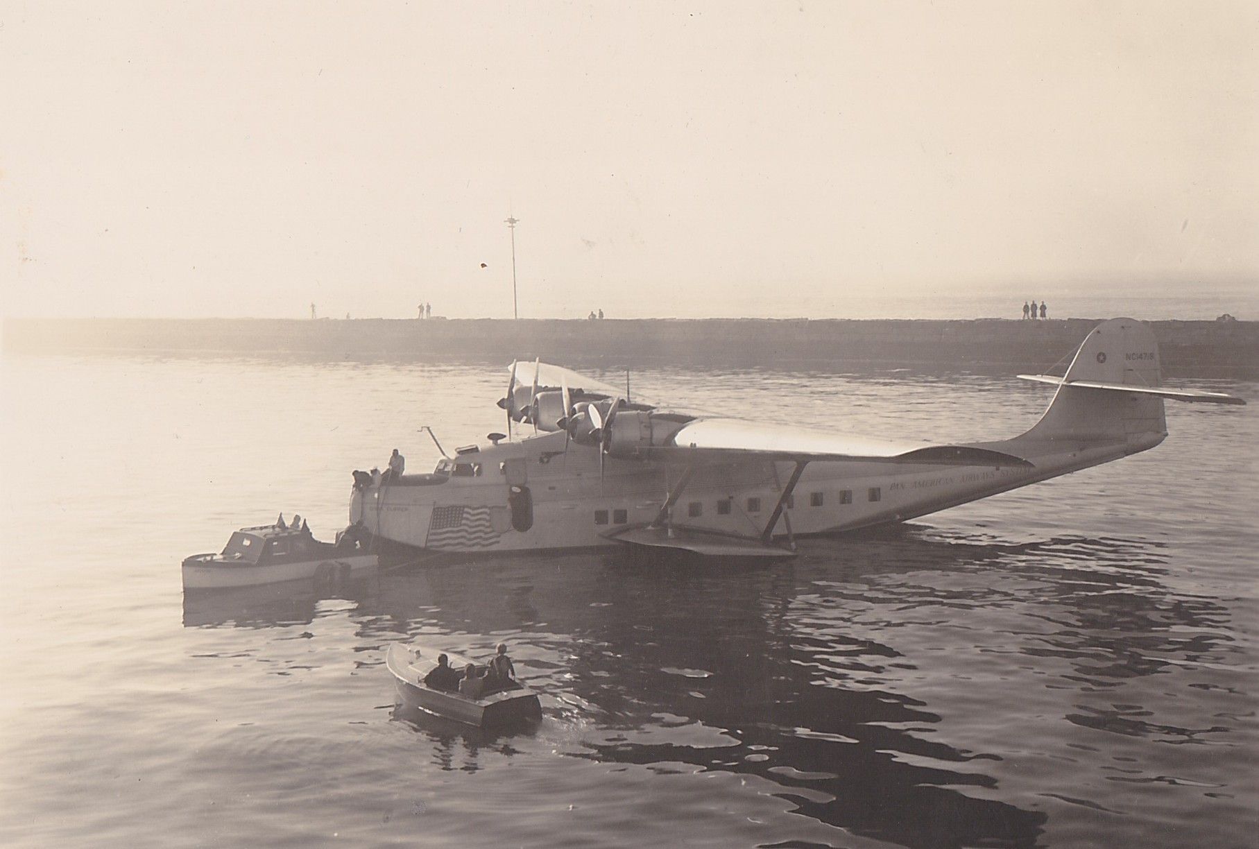 Small boats arrive at the M-130 China Clipper sitting in water.