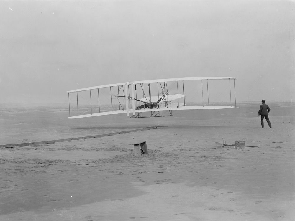 A black and white photo of the Wright Brothers first flight.