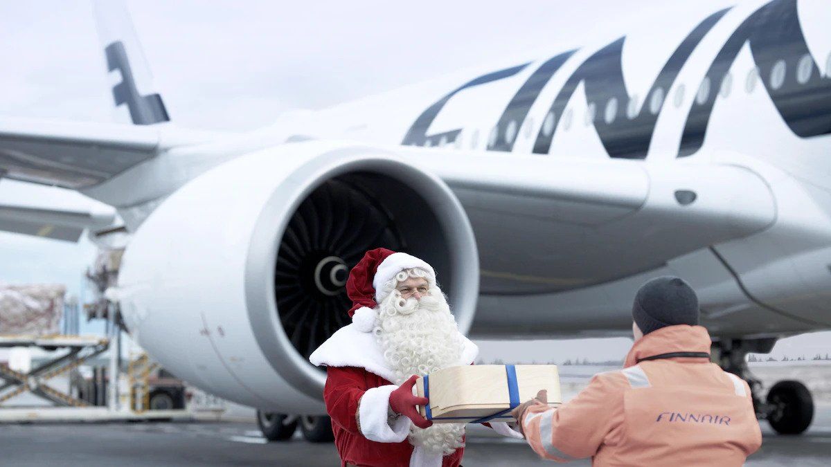 Santa Claus hands a gift to someone in front of a Finnair plane.