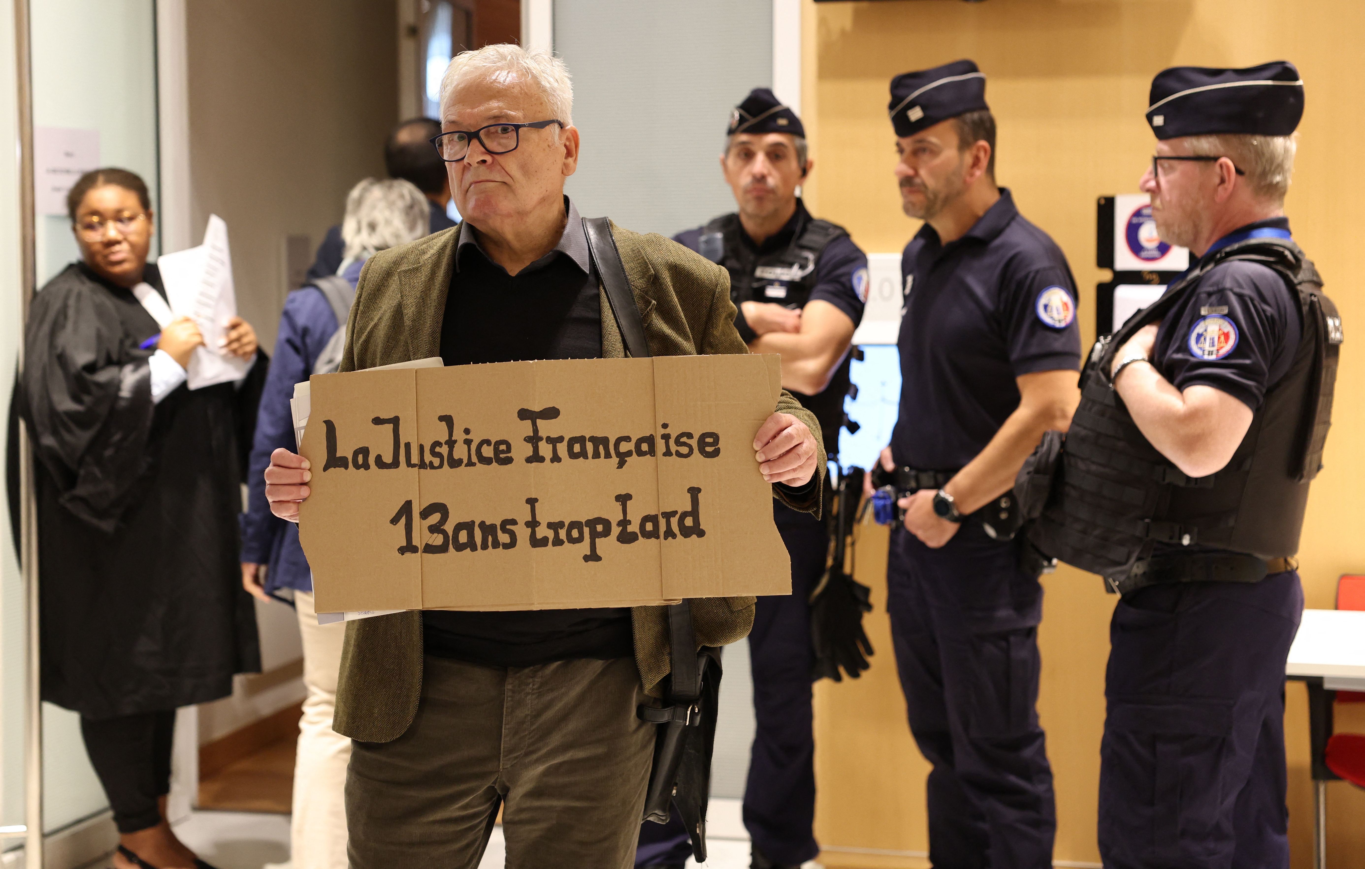 A man holds a placard reading "French justice, 13 years too late" at the Paris courthouse on October 10, 2022 during the trial of Airbus and Air France