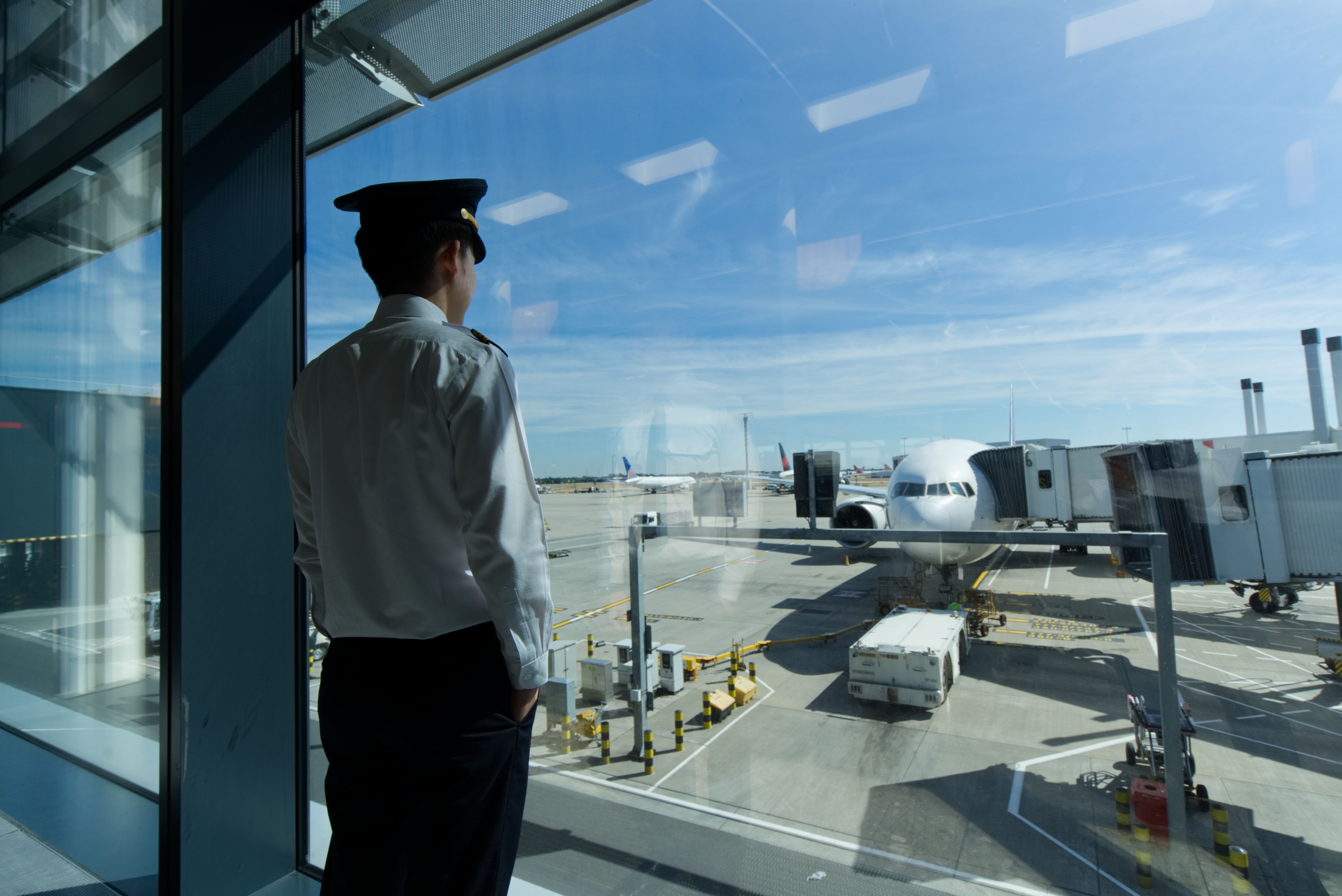 A pilot stands at the boarding gate area in an airport terminal.