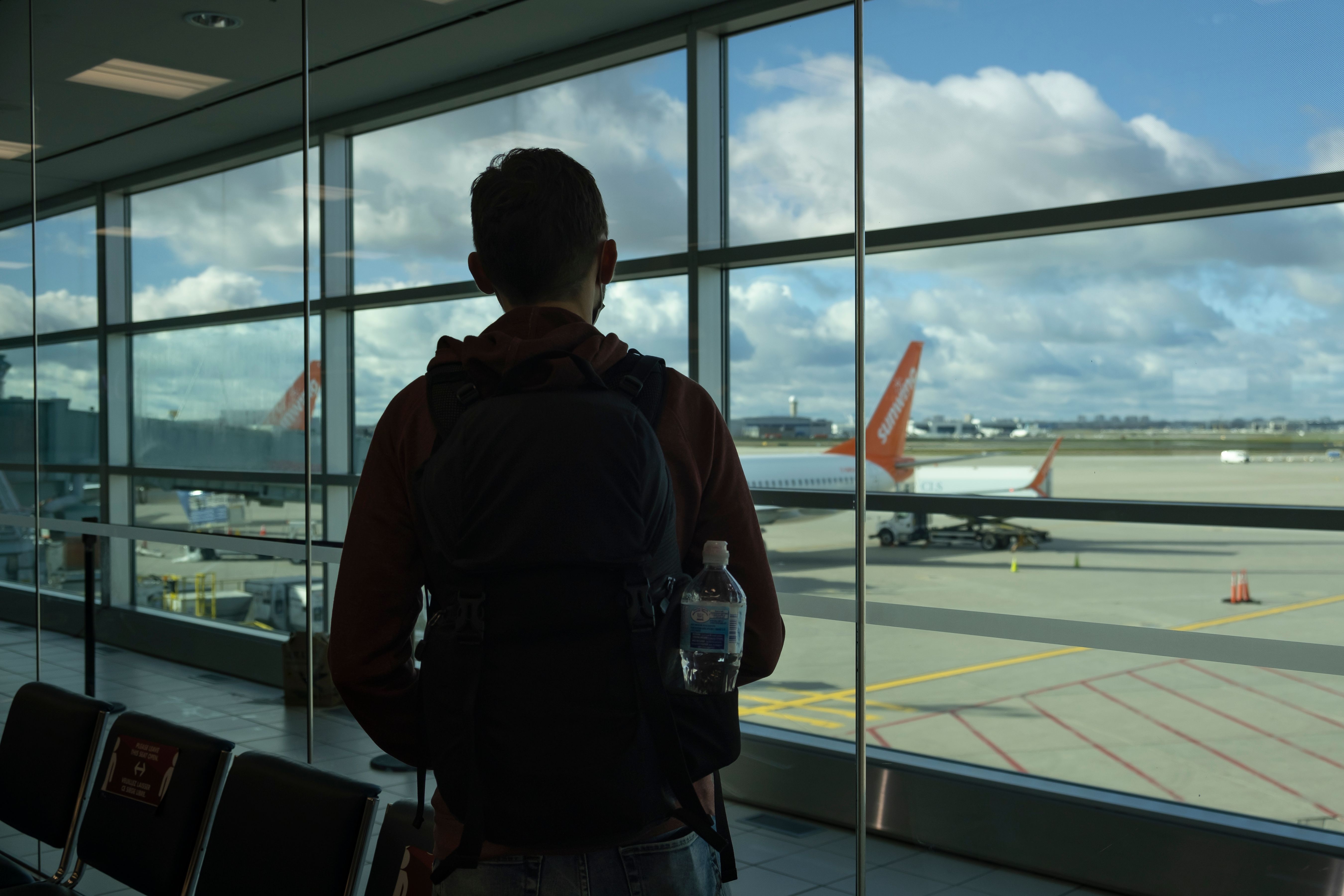shutterstock_2087742370 - Silhouette of young man standing next to window at Pearson International airport, out of focus airplanes and runway in the background. Includes Sunwing Airline Boeing 737