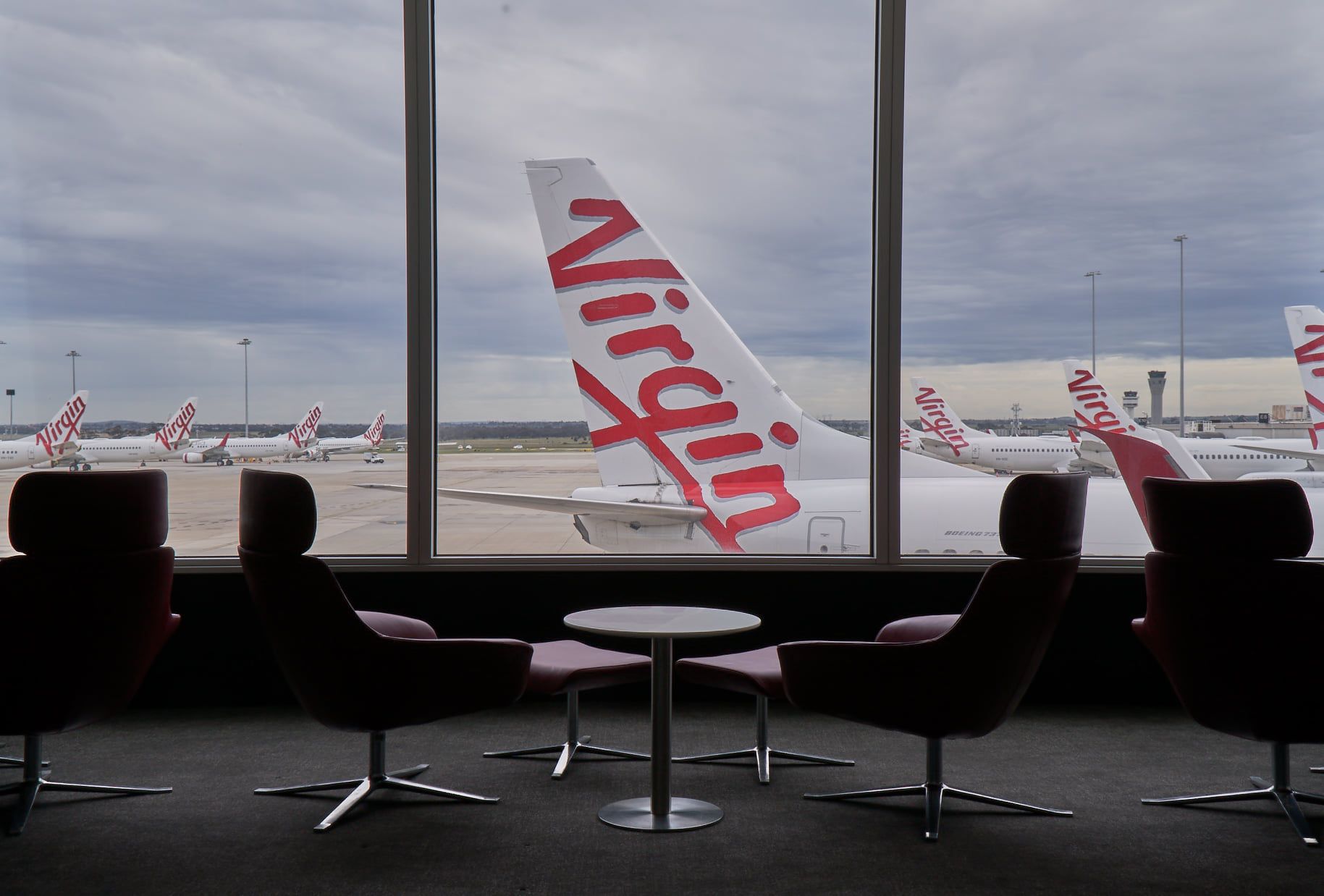 A Virgin Australia Boeing 737 tail seen through an airport terminal window.