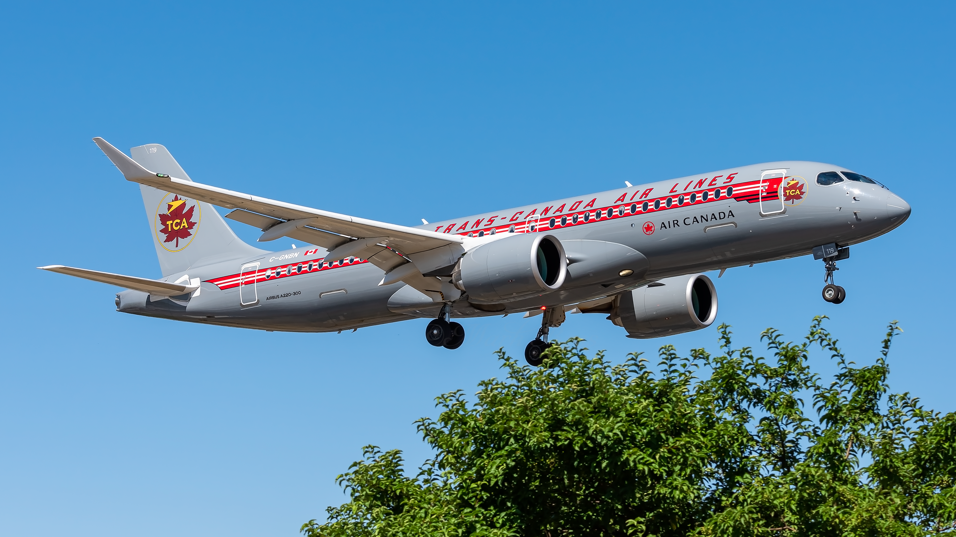 An Air Canada A220 in retro livery flying in the sky.