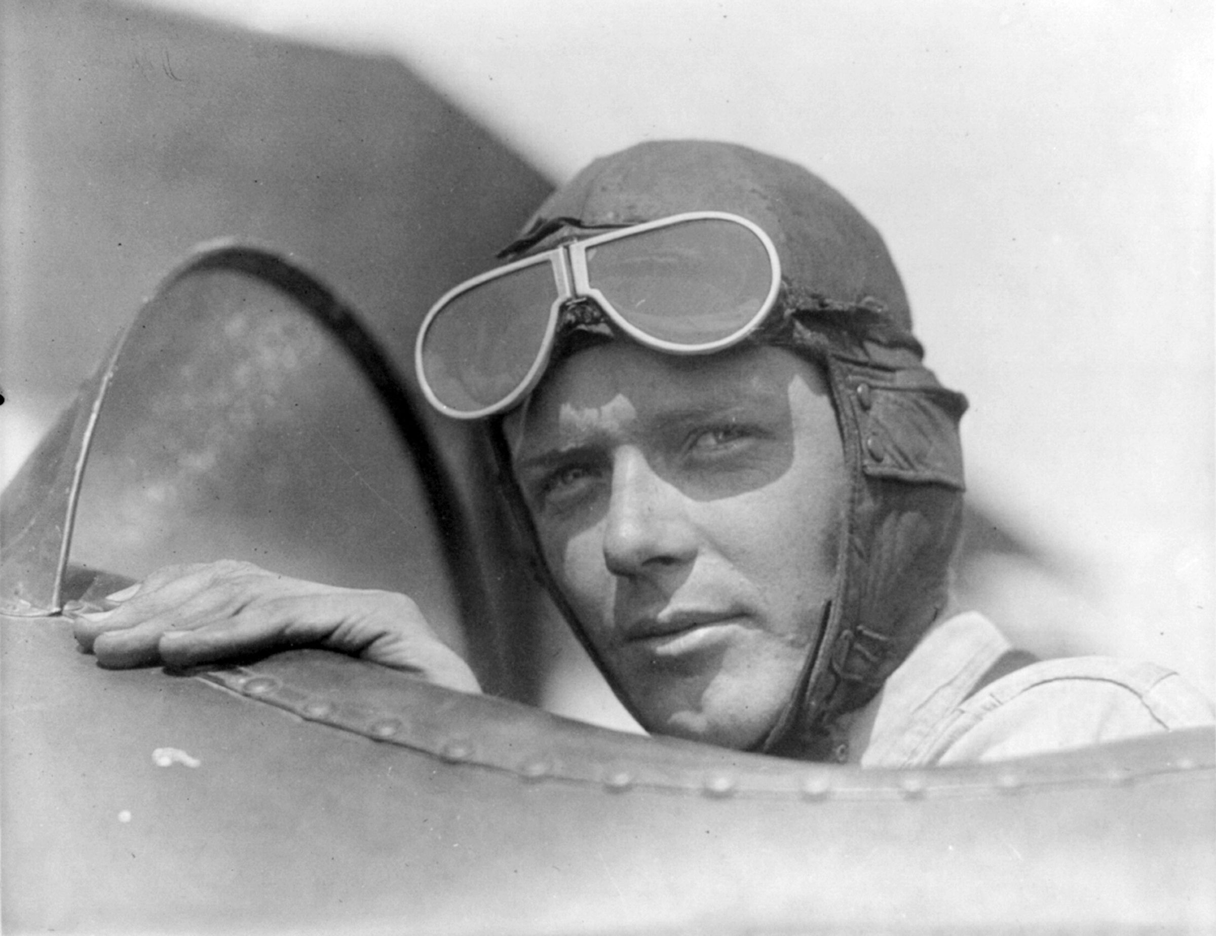 Vintage photo of a man wearing an aviator's cap and goggles looking out the cockpit of an early aircraft