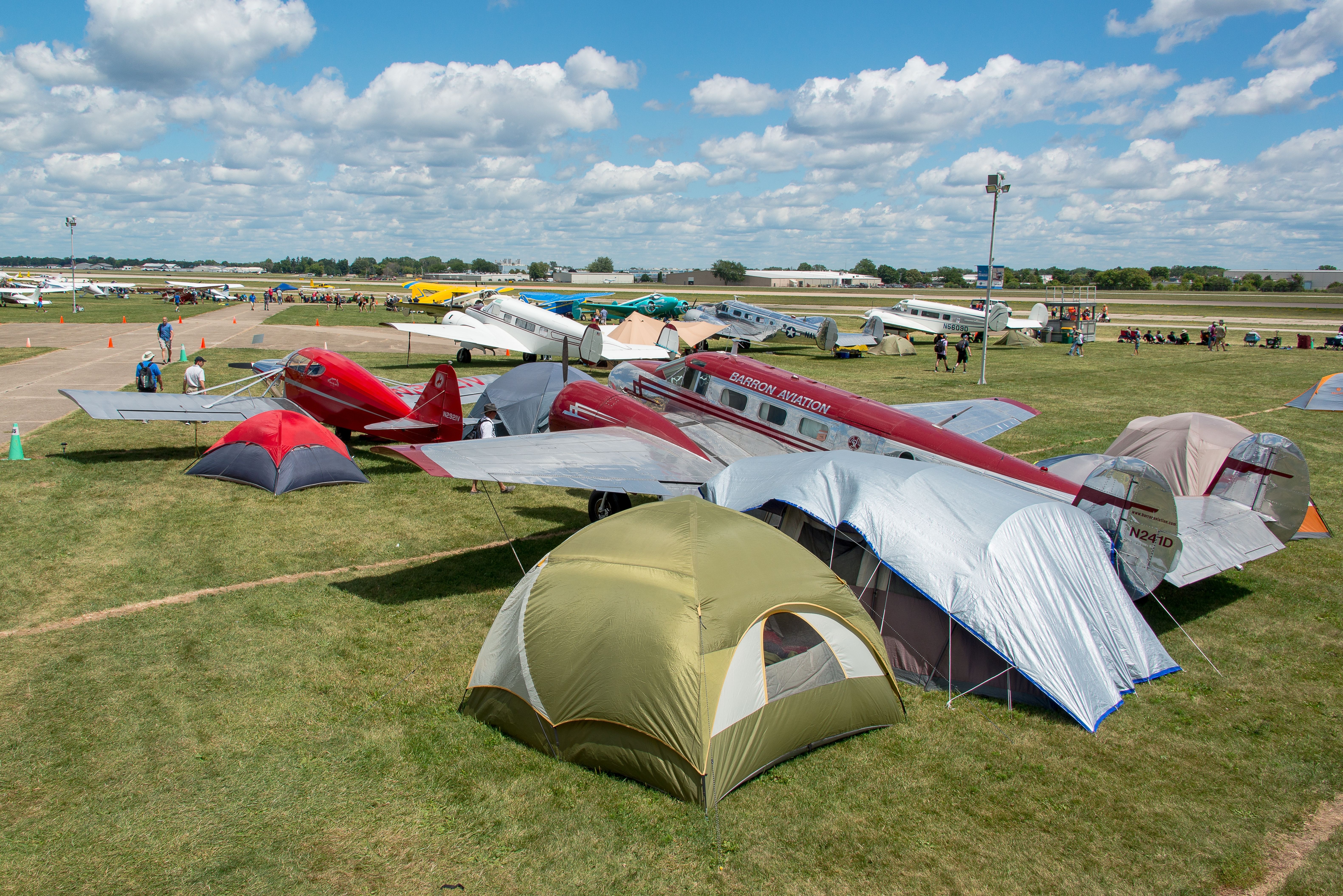 Multiple general aviation aircraft parked outside tents in a field. 